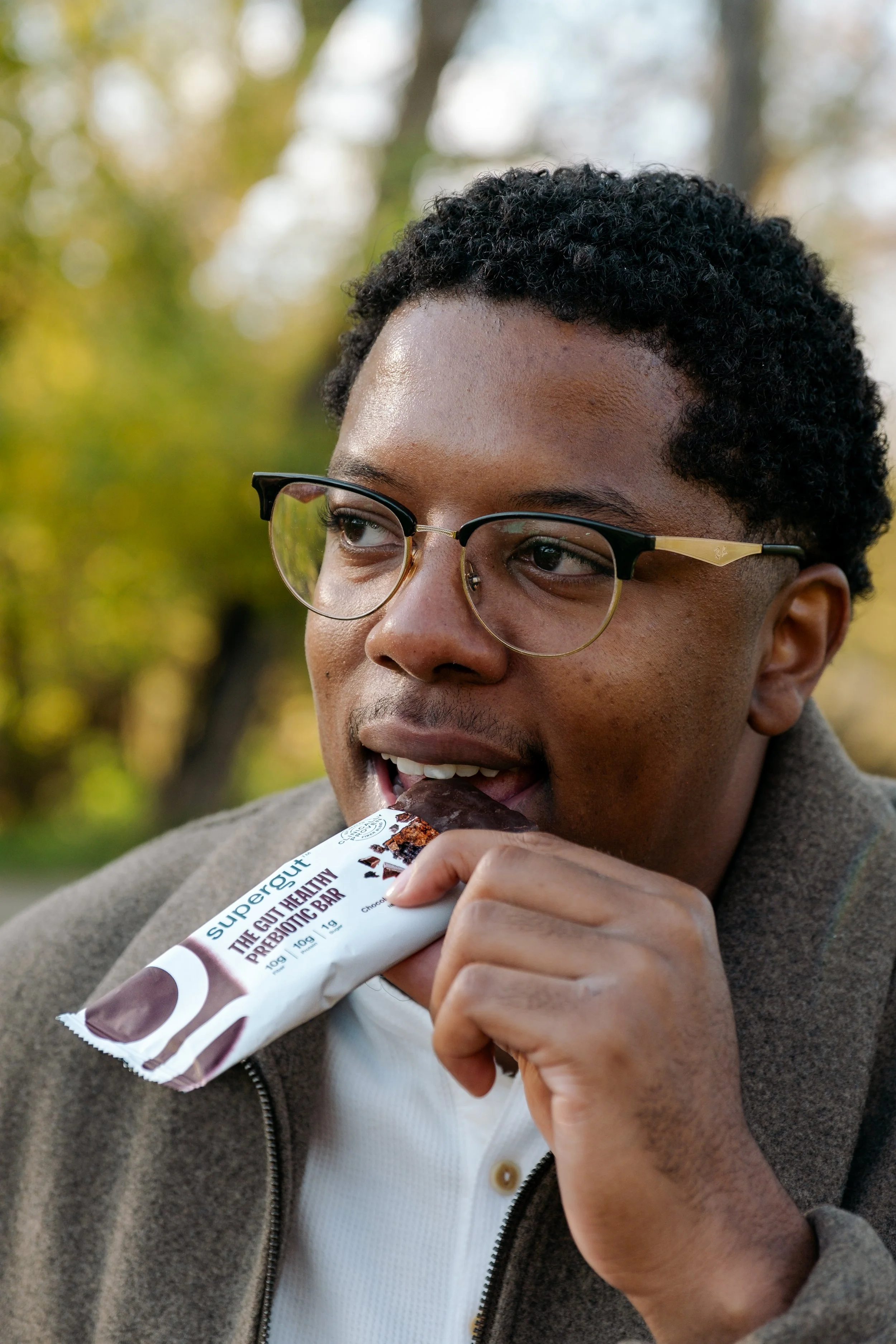 Black man eating Supergut bar outdoors.