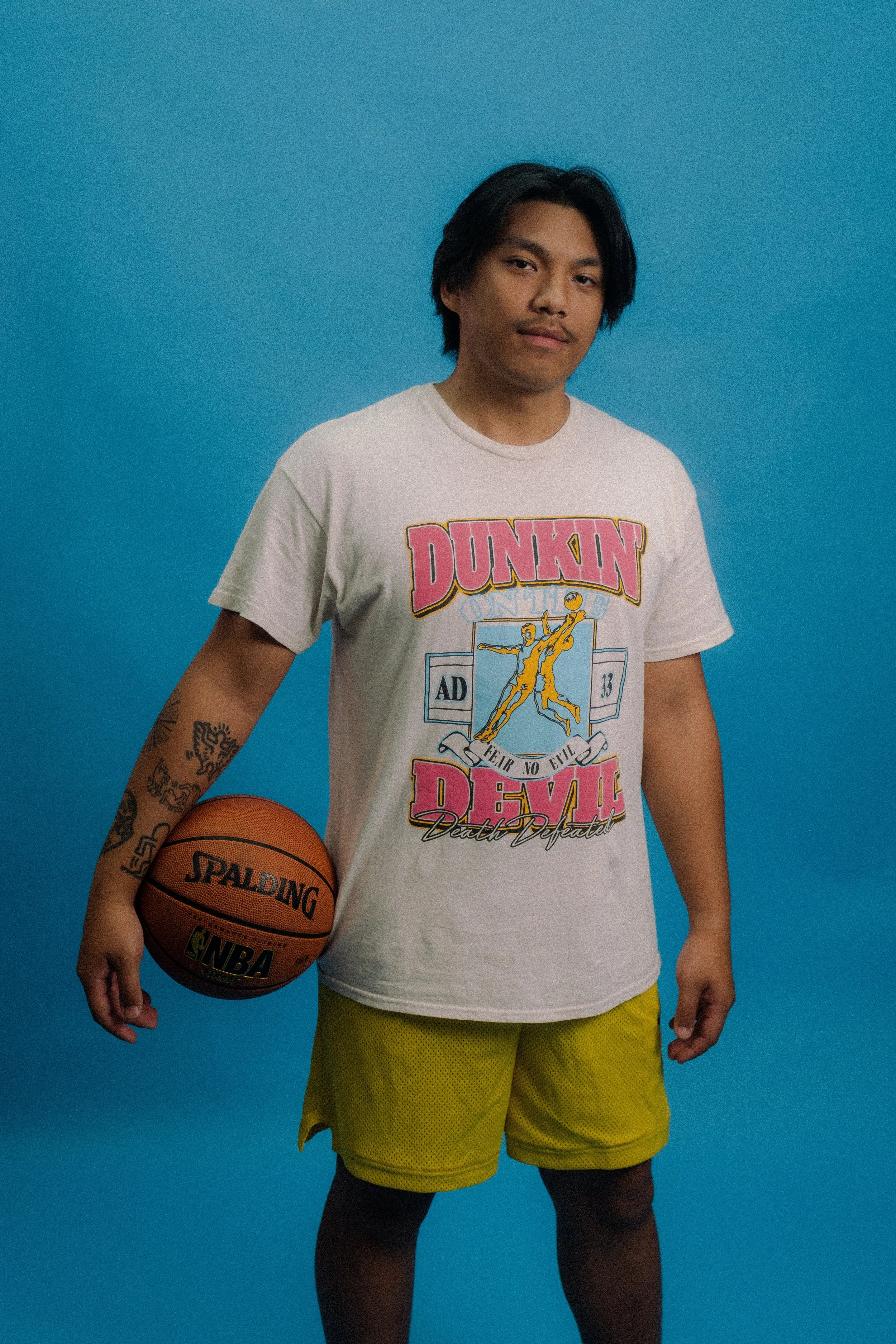 Man modeling vintage shirt against blue backdrop with basketball in hand.