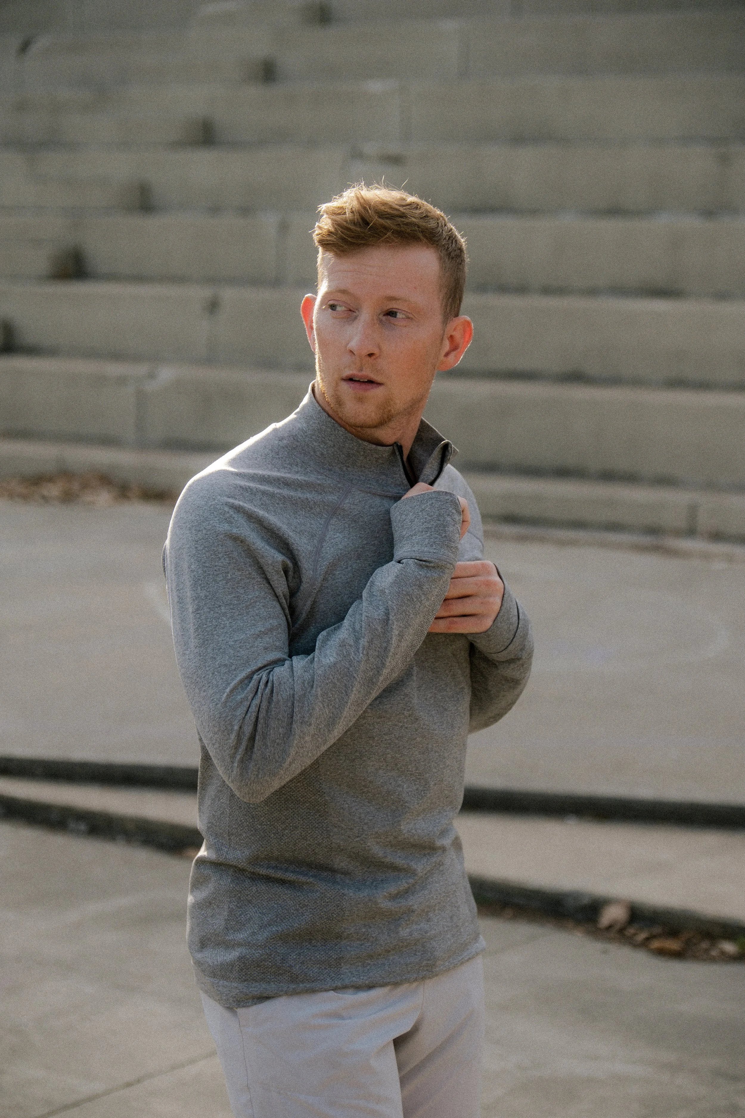 Man zipping up grey long sleeve quarter zip jacket and looking over his shoulder.