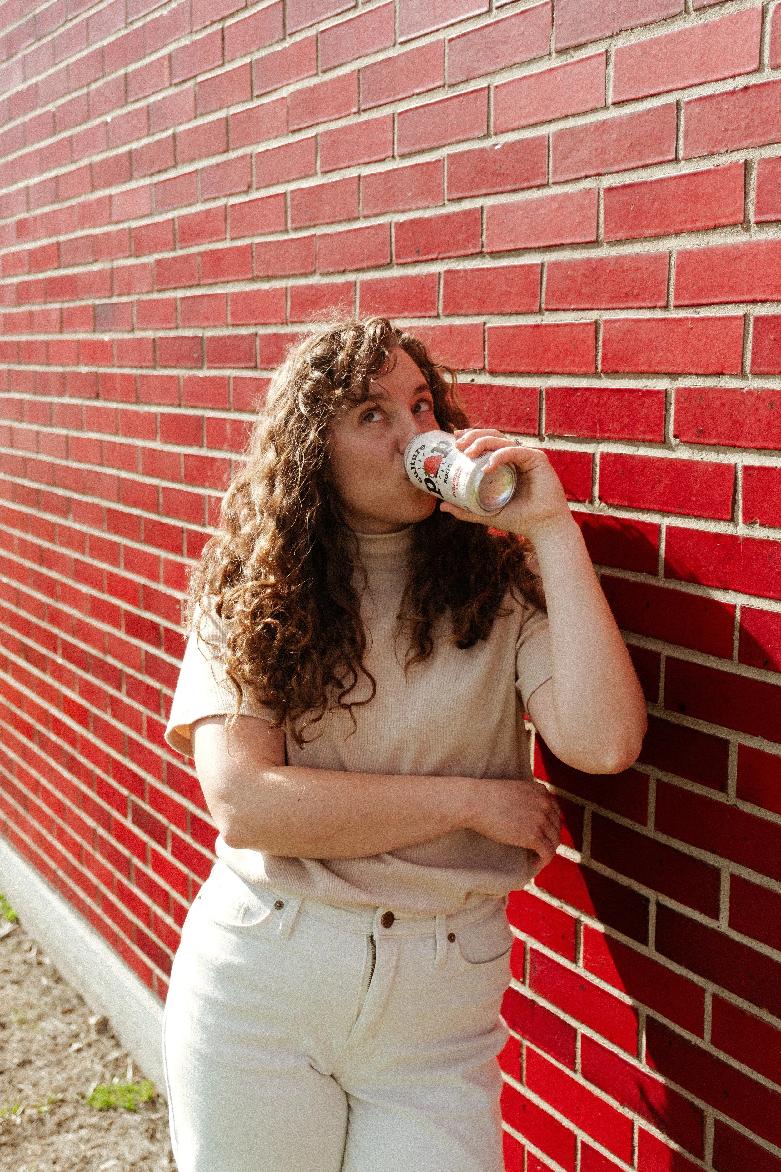 Girl drinking Culture Pop Soda against a red brick wall