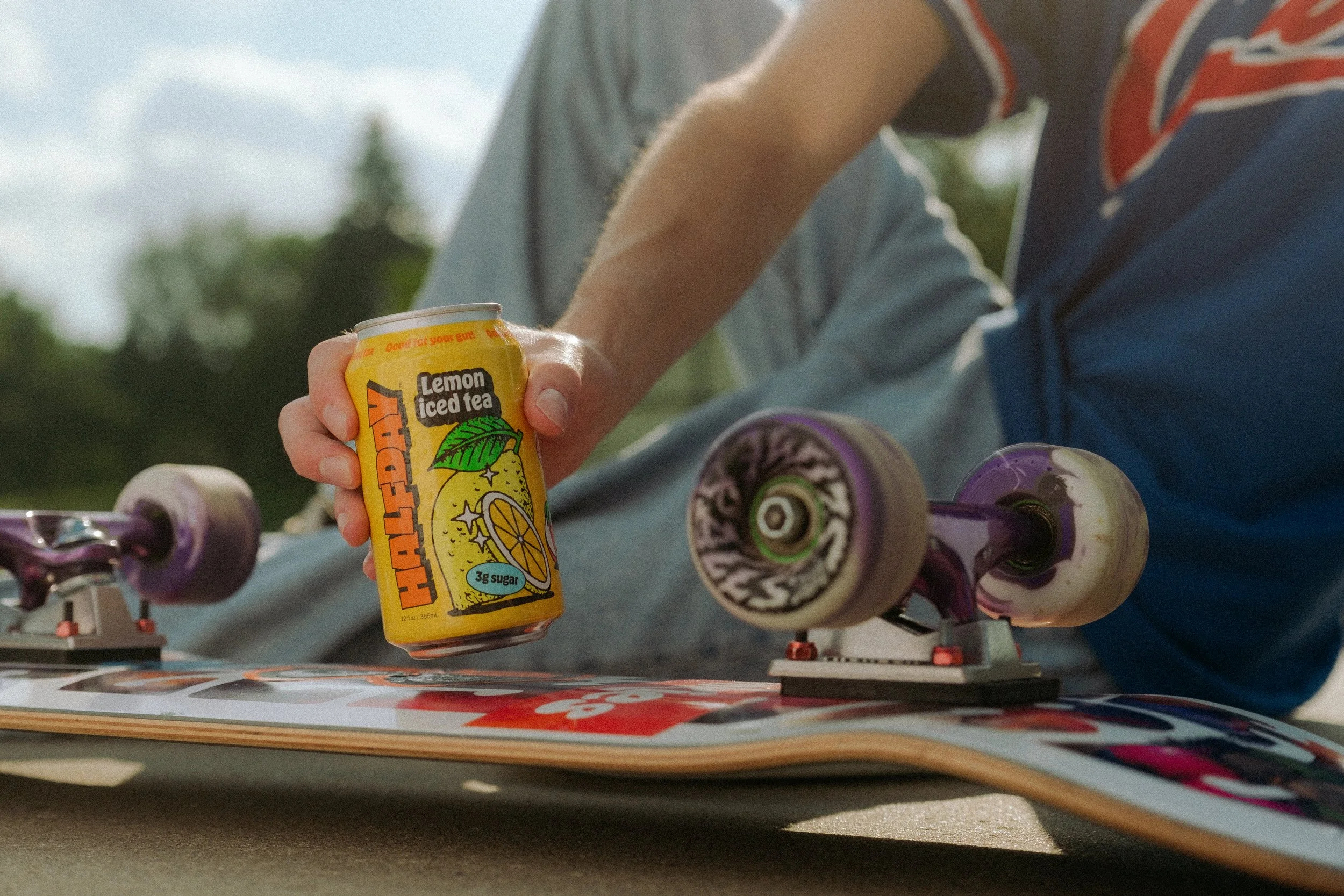 Man's hand grabbing Halfday Iced Tea on skateboard.