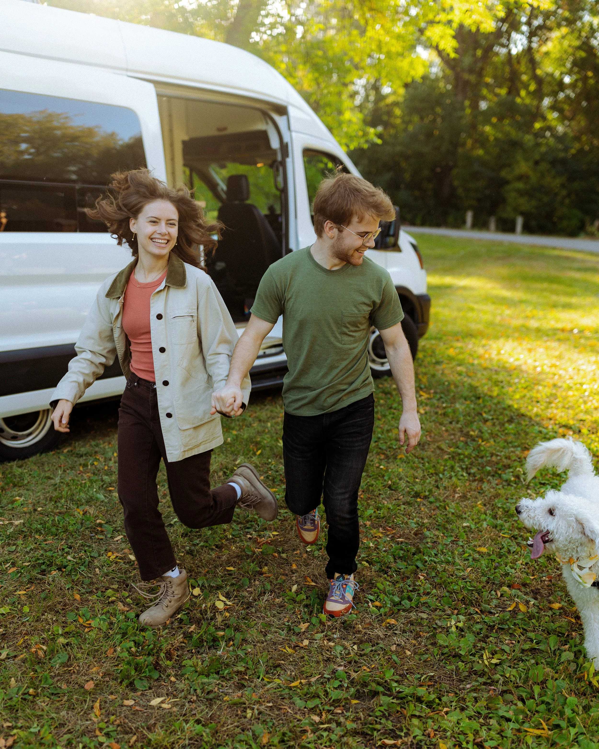 Man and woman running outside with their dog, with van in the background.