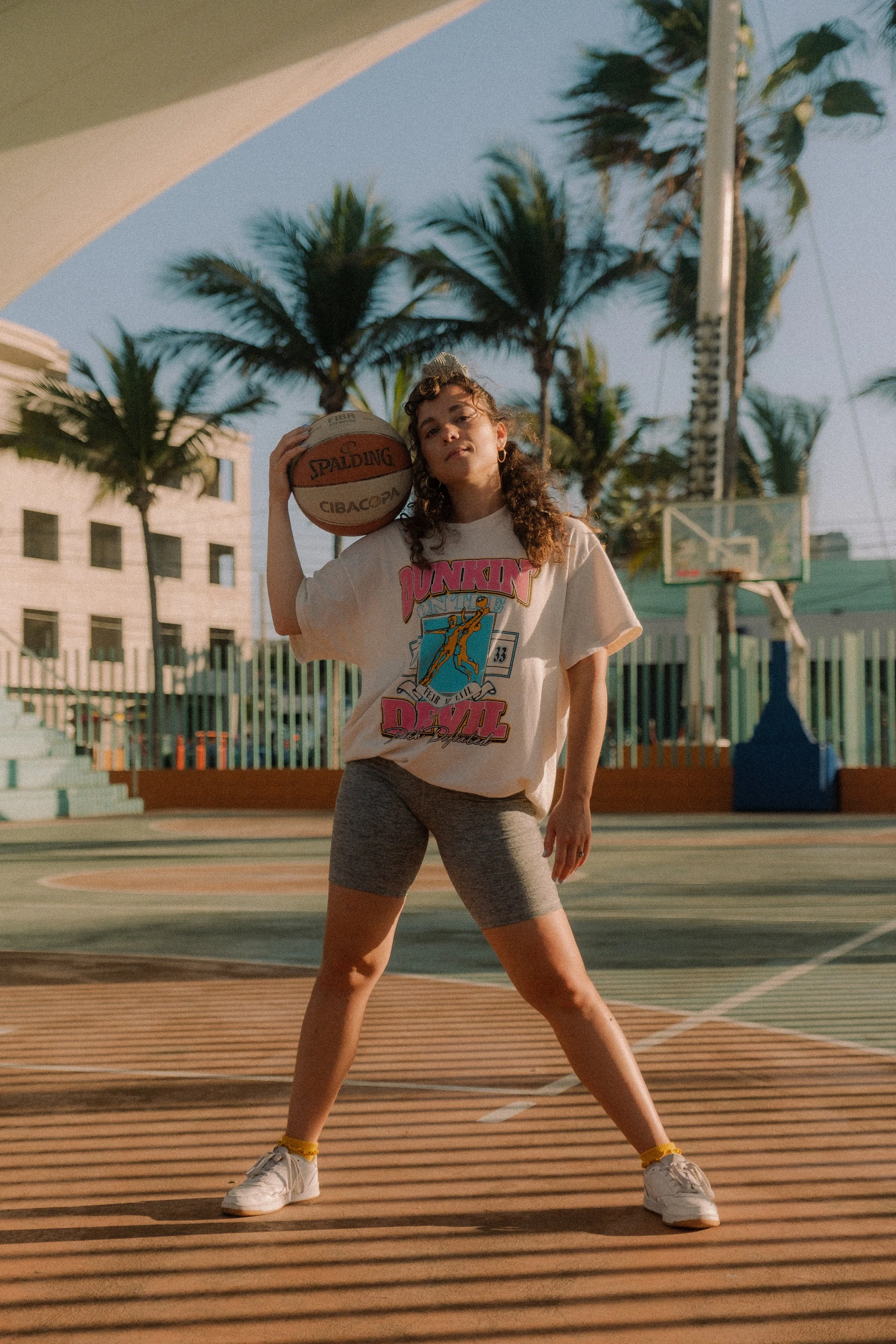 Woman posing with basketball on an outdoor basketball court.