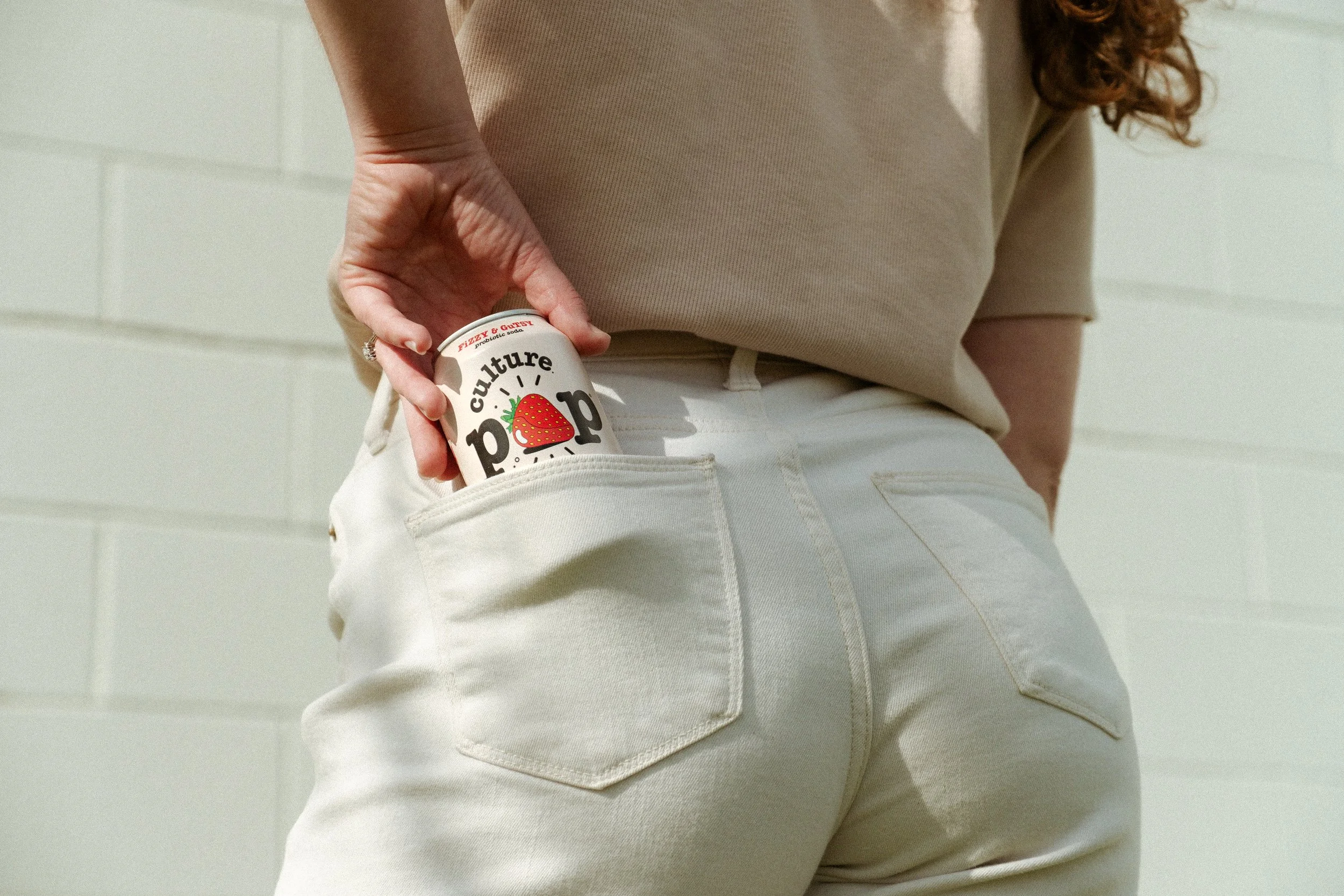 Girl reaching into back pants pocket to grab Culture Pop Soda