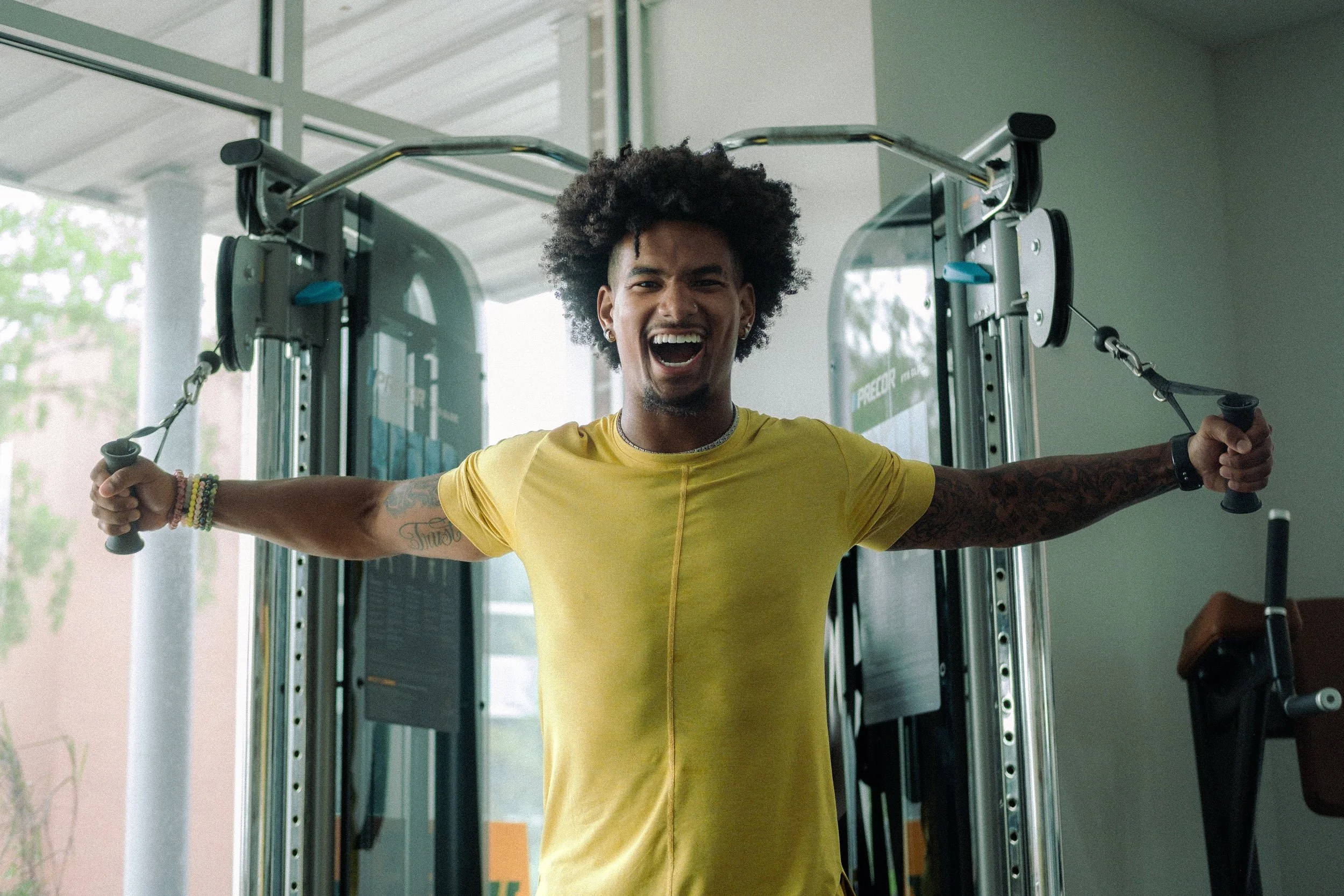 Black man with yellow shirt doing cable fly exercise.