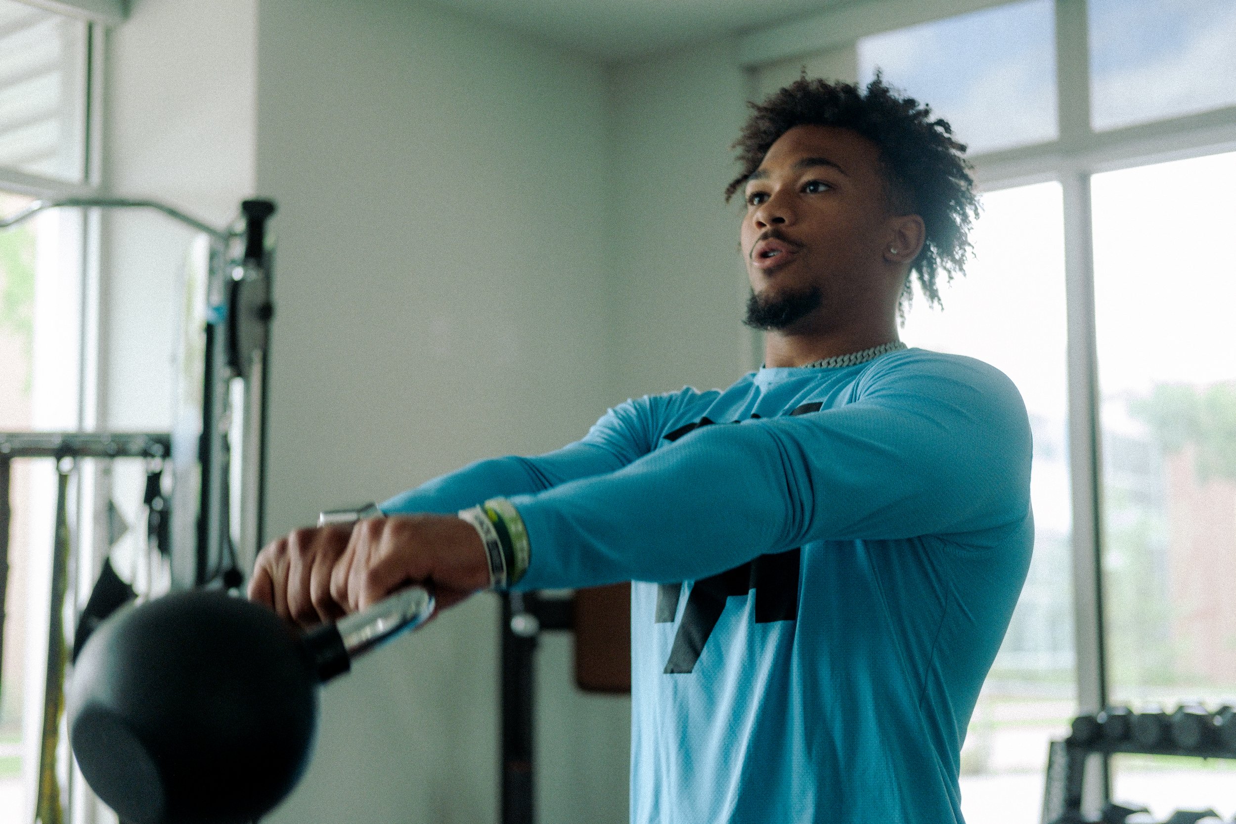 Black man in blue shirt swinging kettle bell.