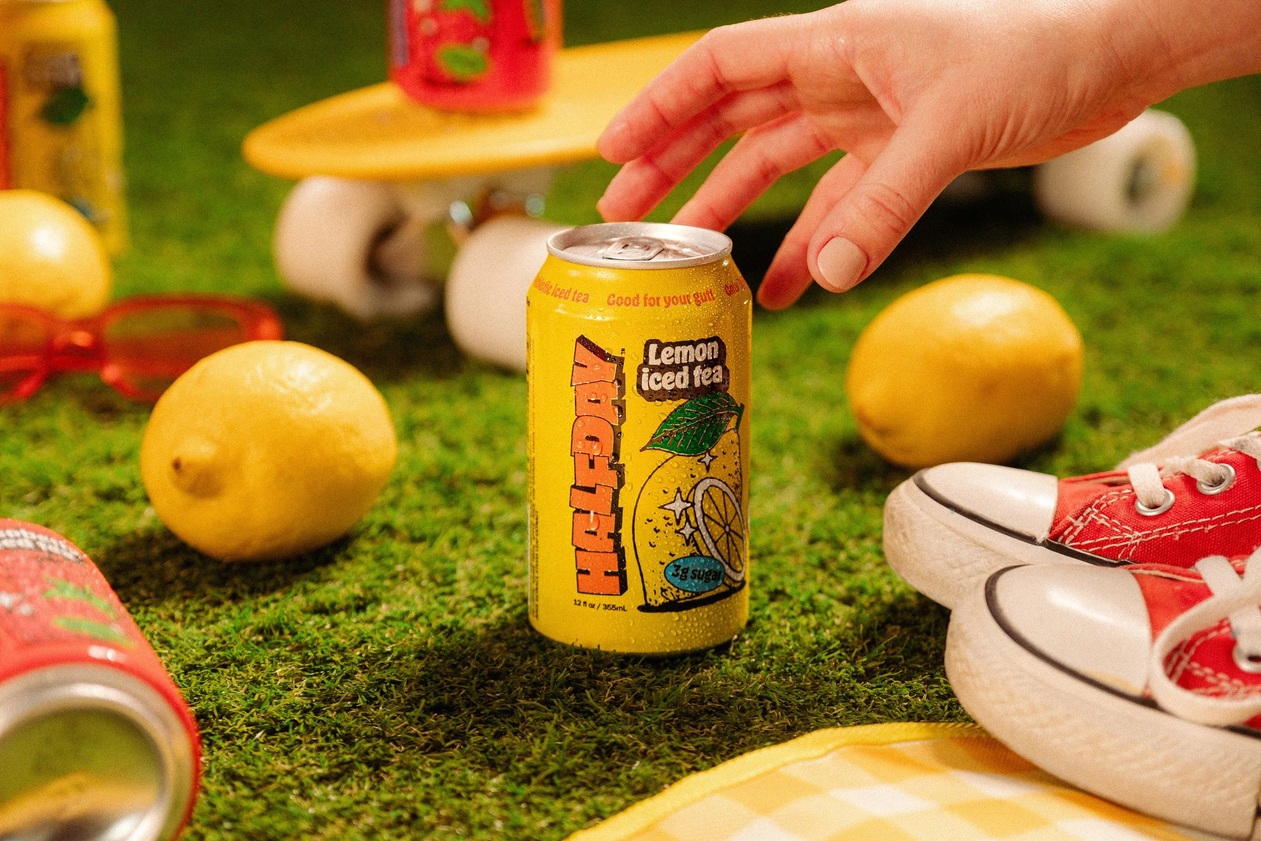 Female hand reaching for lemon Halfday Iced Tea with yellow penny board in background.