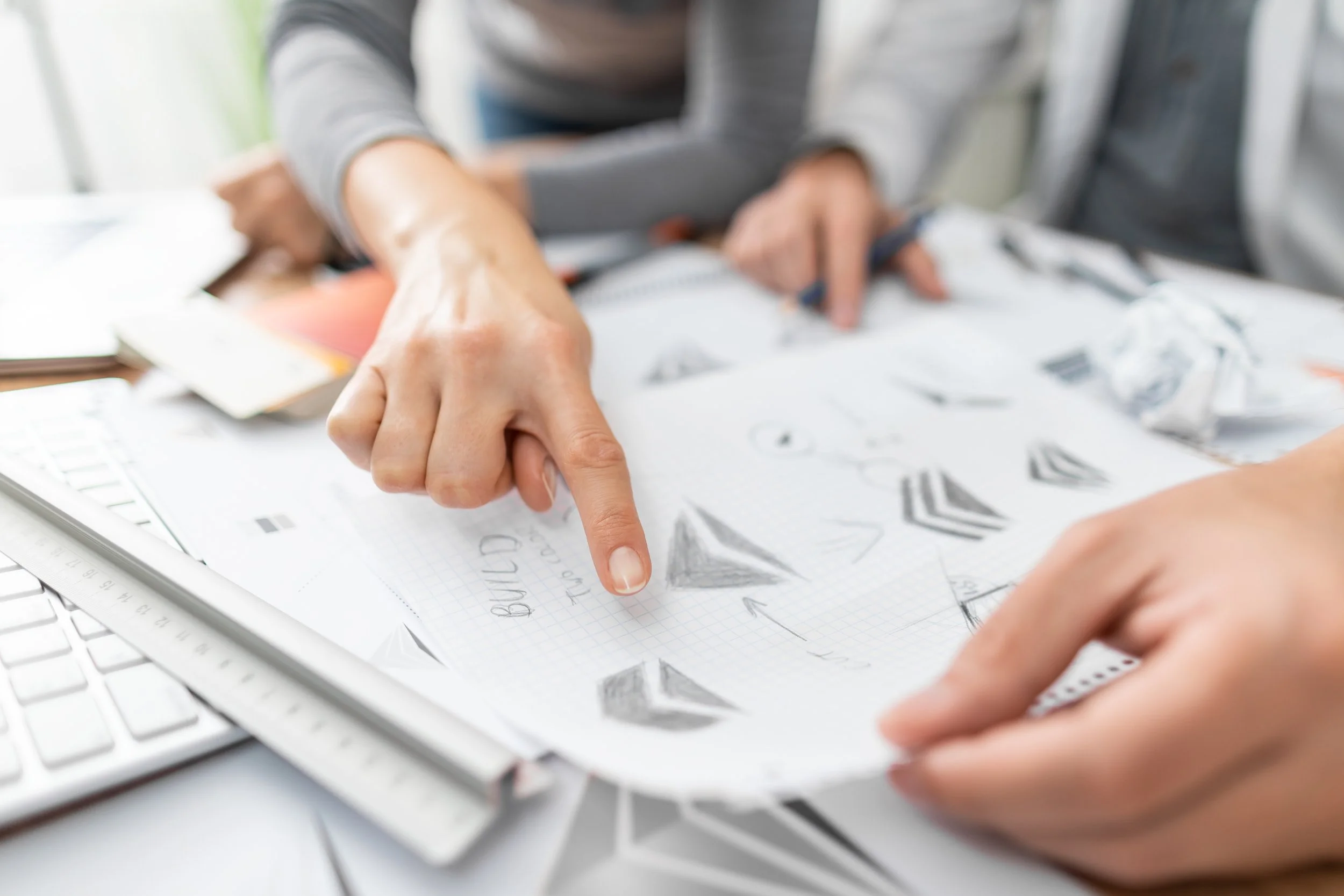 Hands pointing to hand-drawn logo sketches during a branding discovery session, representing collaborative design exploration.