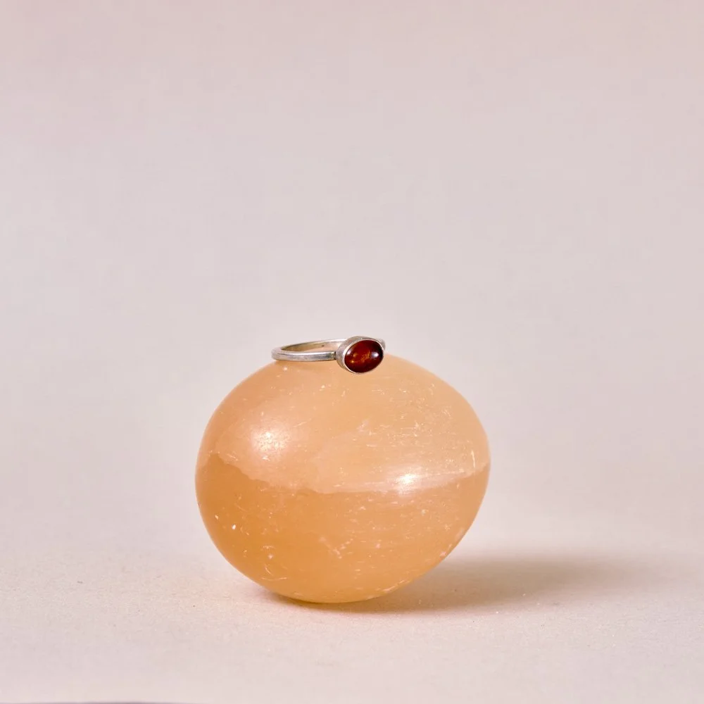 A silver ring with a red gemstone resting on a round salt lamp with a pinkish hue.