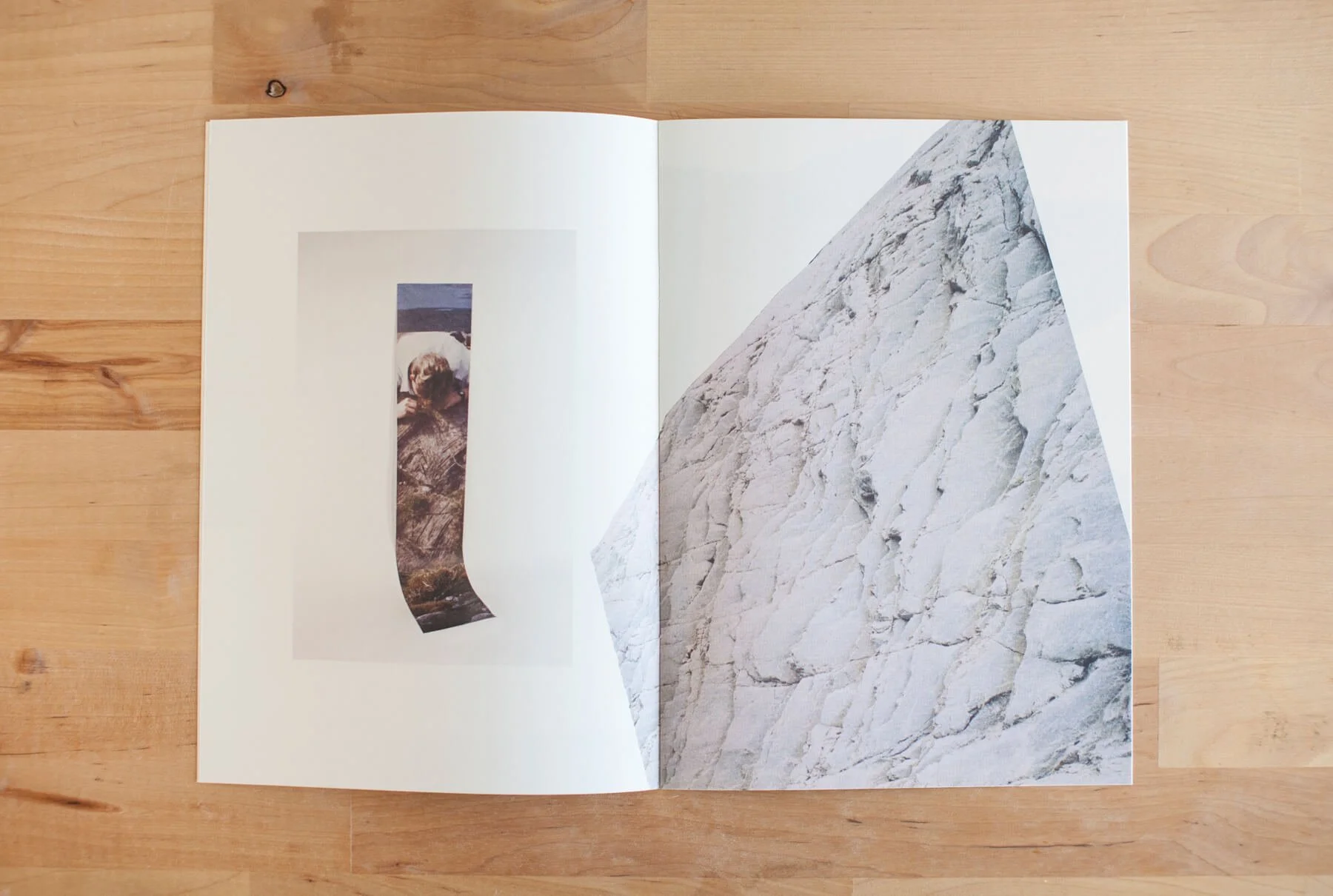 Open book on wooden surface showing a collage of a mountain and a person looking over rocks, with the mountain image appearing as if it is folding.