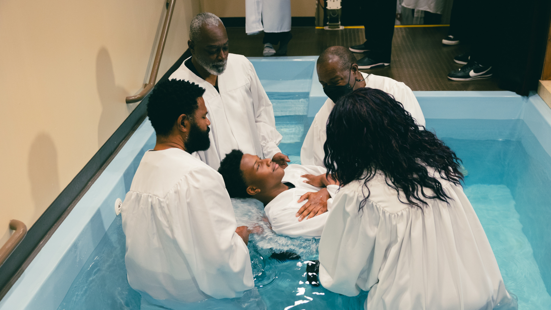 Young man smiling in a park on a sunny day, wearing a light gray t-shirt, with trees and grass in the background.