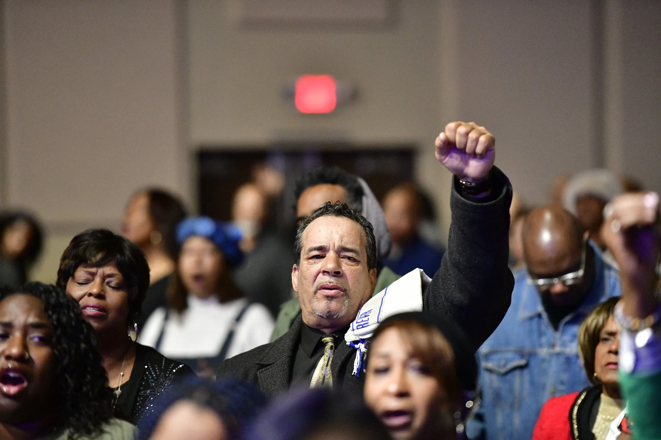 Three people smiling in a bright, decorated room with hanging plants and shelves.