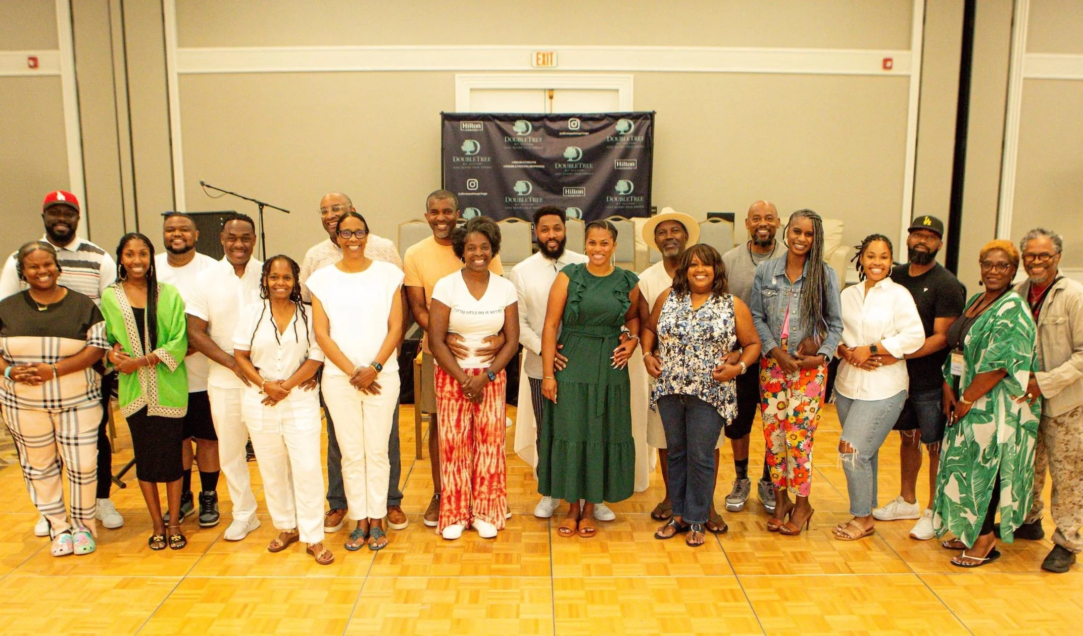 A smiling man and woman sitting closely together on a bed, with the woman resting her hand on the man's shoulder.