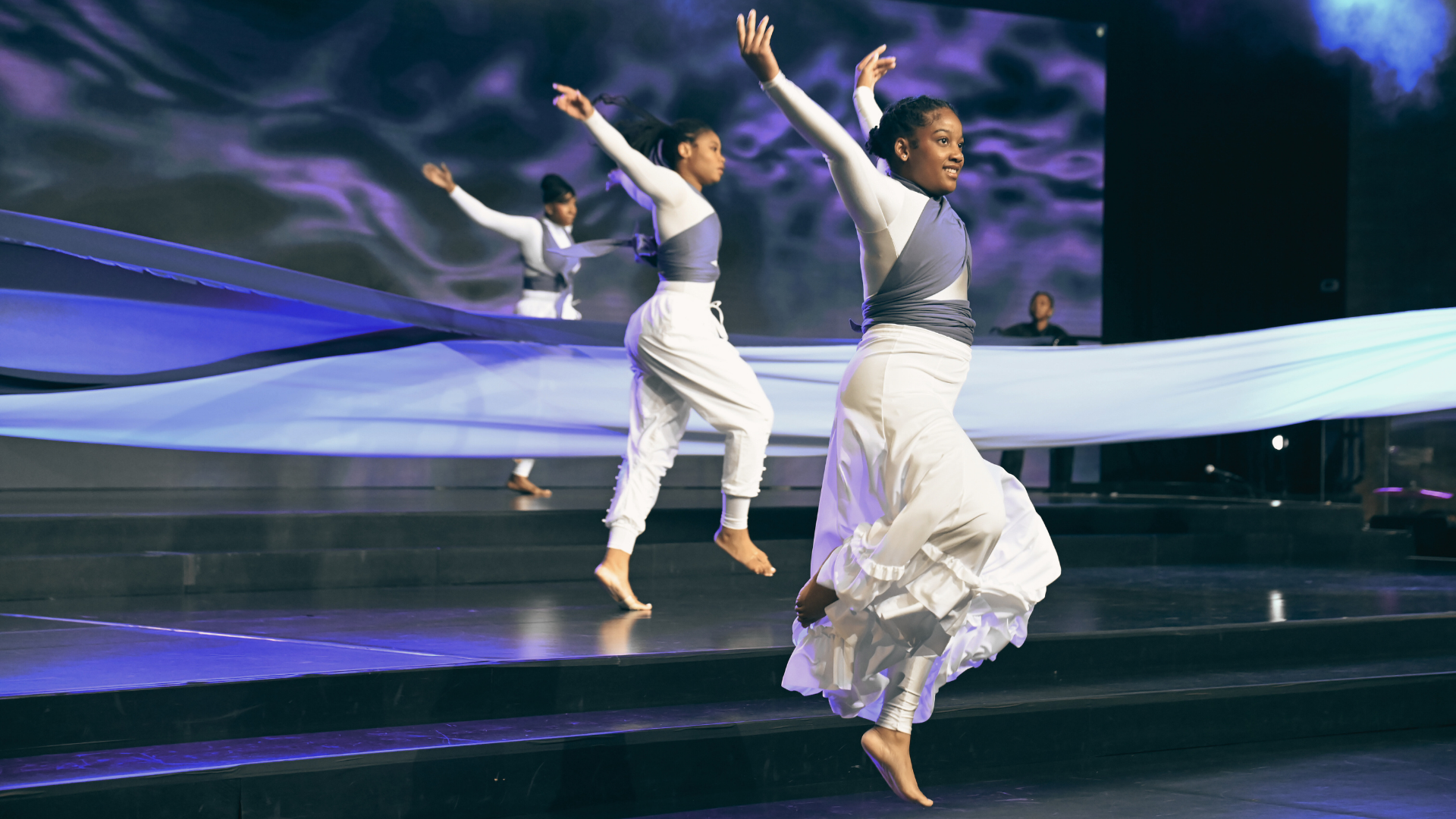 Group of six diverse teenagers sitting on outdoor steps, smiling and looking at the camera.
