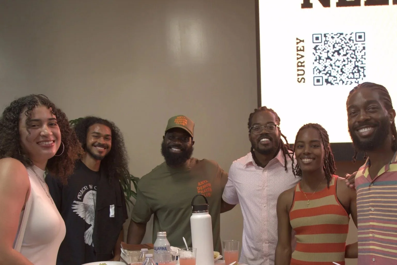 Three young adults walking outdoors against a reddish-brown wall, talking and smiling.