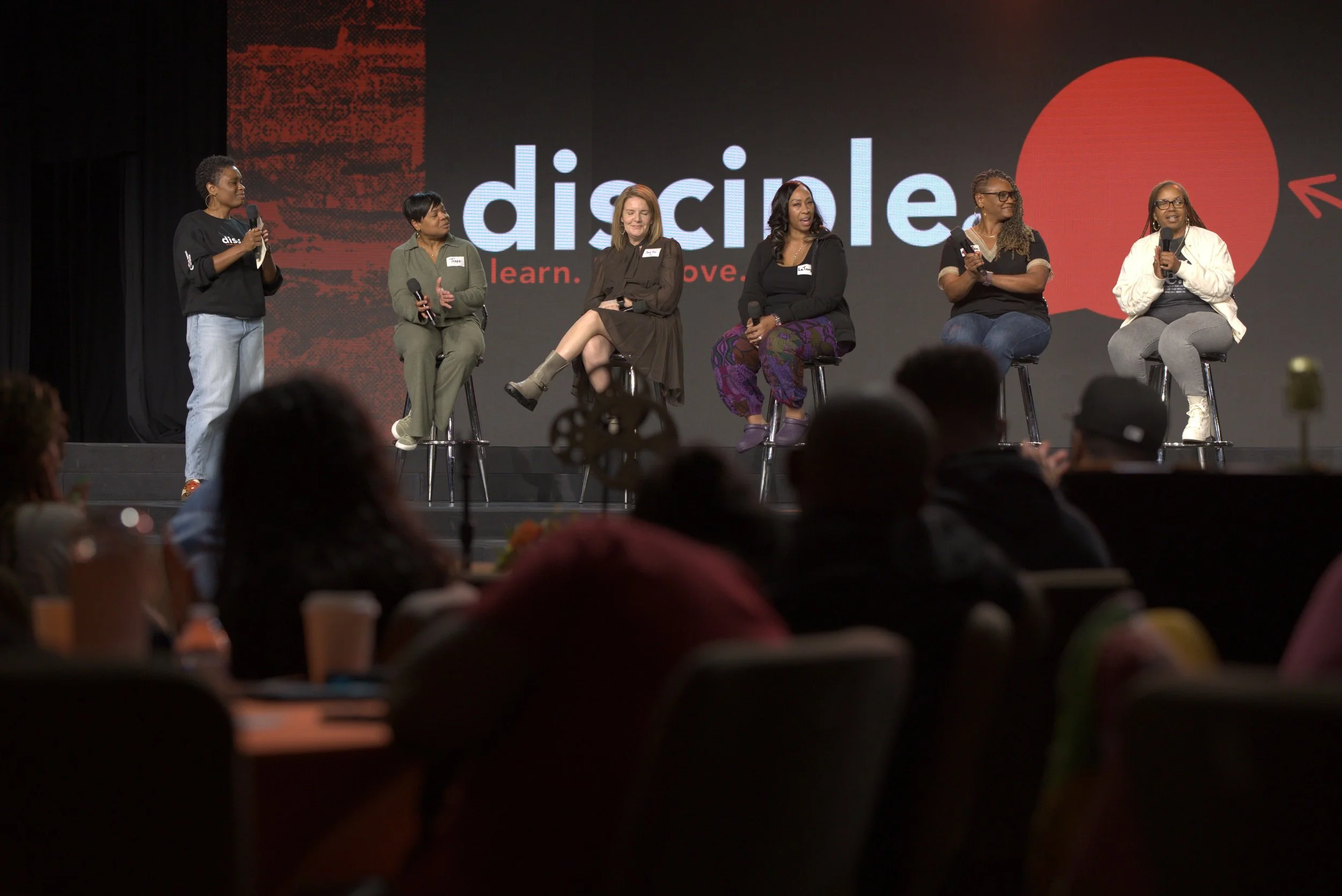 Group of diverse people standing in a circle with hands stacked in the middle, smiling and celebrating outdoors under a clear sky.