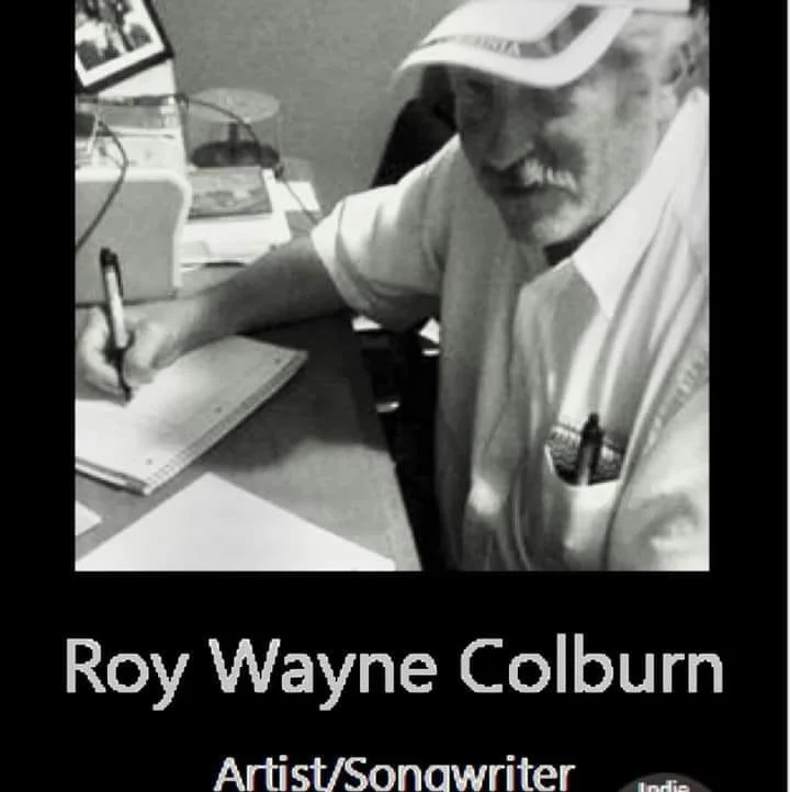 Black and white photo of Roy Wayne Colburn, an artist and songwriter, sitting at a desk, writing in a notebook, with various items on the desk. His name is displayed below the photo.
