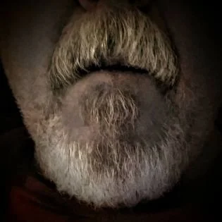 Close-up of Kim Kimbo Groff's face with a prominent gray beard and mustache, and short hair with a distinct hairstyle.