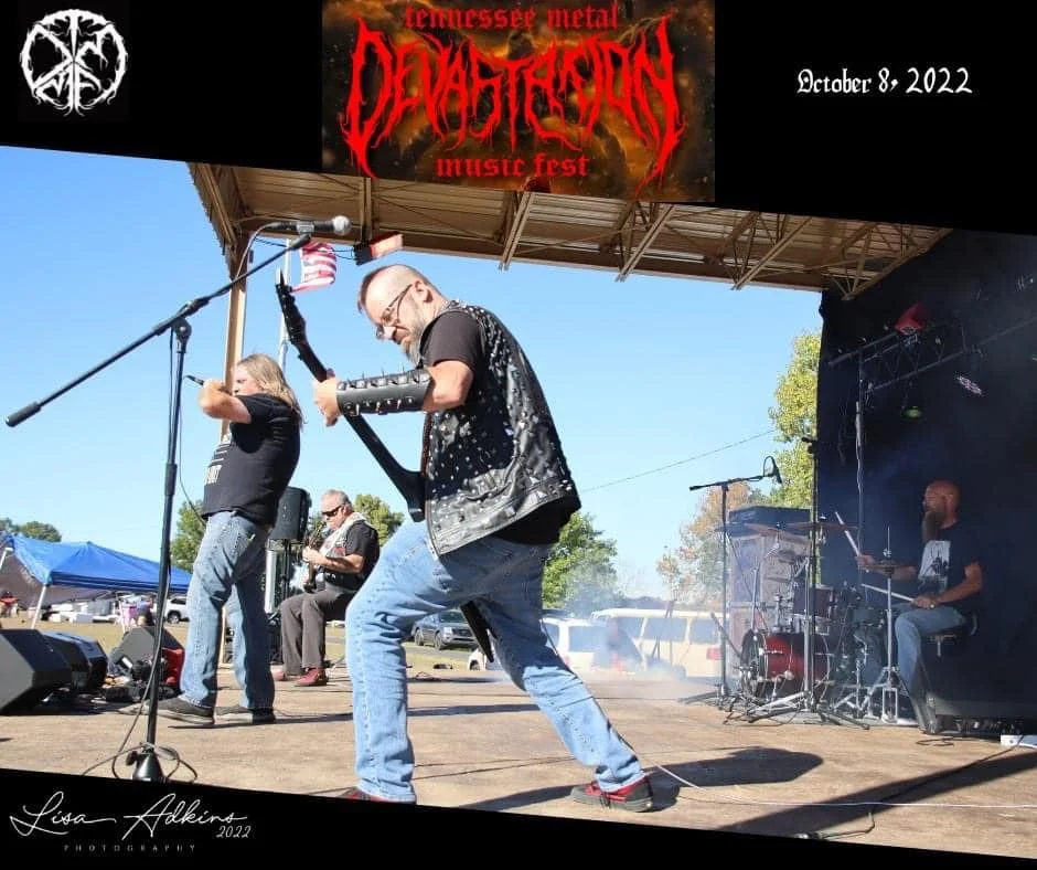 A band performs on stage at the Tennessee Metal Devastation Music Fest on October 8, 2022. The lead guitarist wears a black shirt, jeans, and a studded arm sleeve, while a vocalist with long hair and a black shirt sings into a microphone. A drummer i