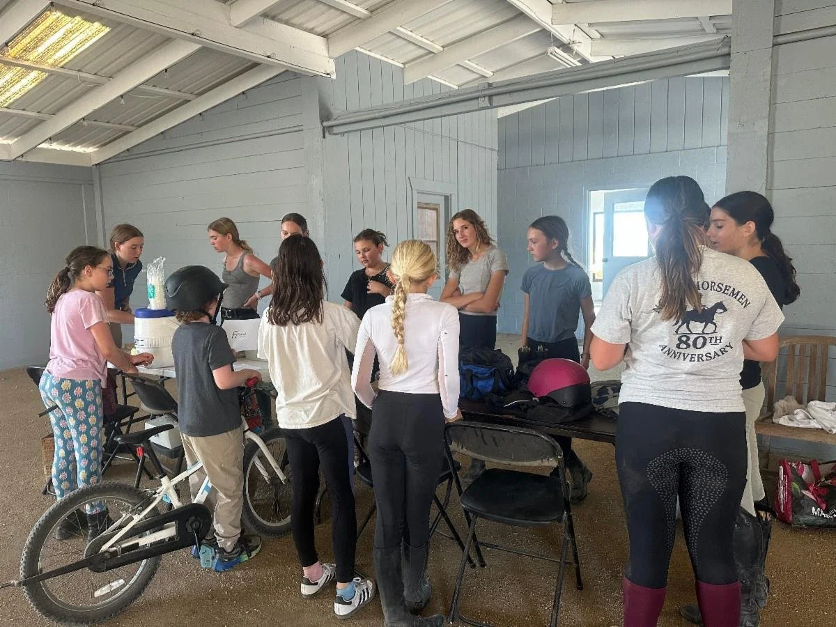 Group of young riders gathered indoors during Strides Riding Academy Mini Horse Camp in Santa Rosa, learning horse care and teamwork.