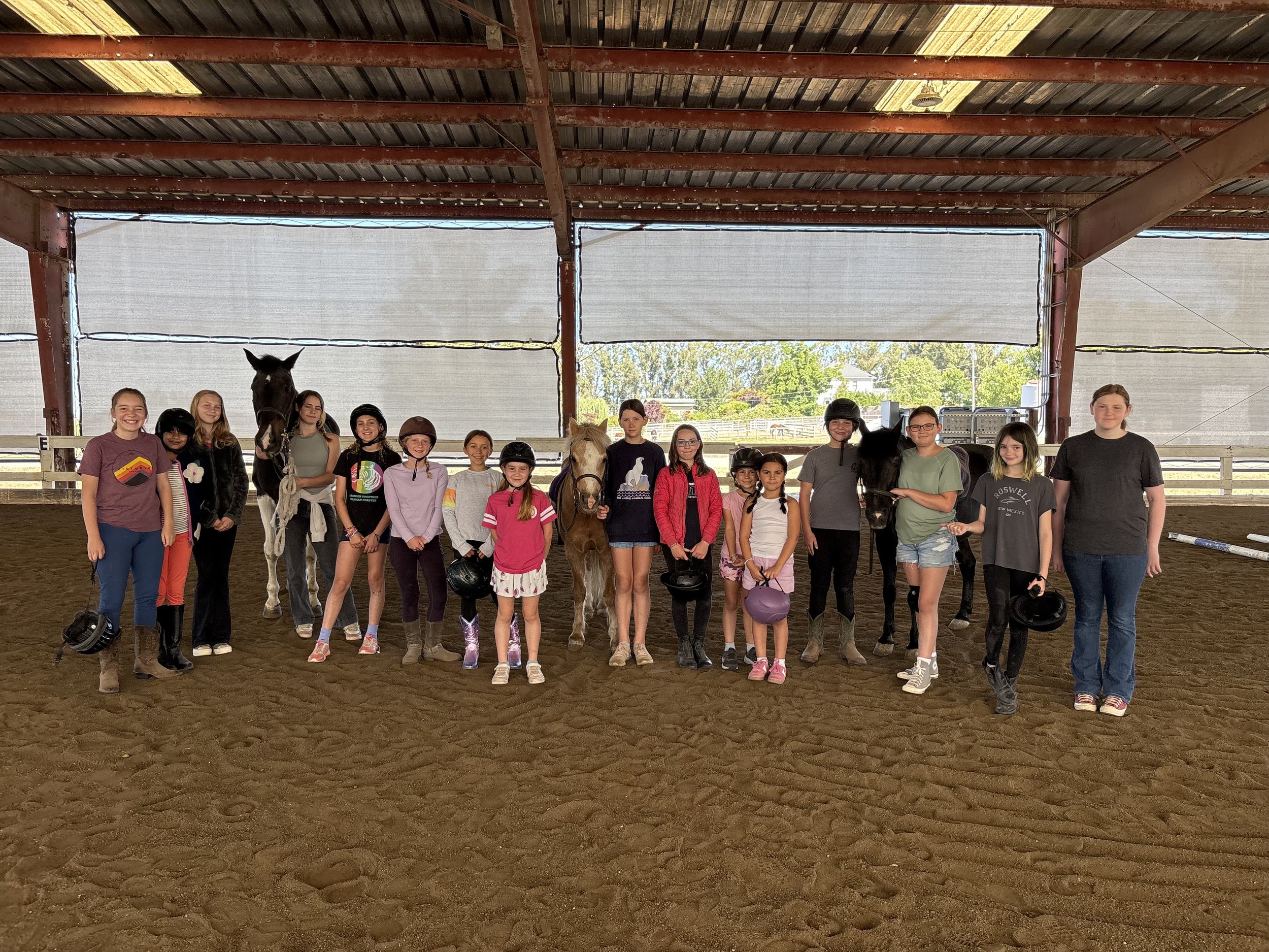 Group of smiling campers at Strides Summer Camp in Sonoma County, some standing and some on horseback, enjoying time together at the barn.