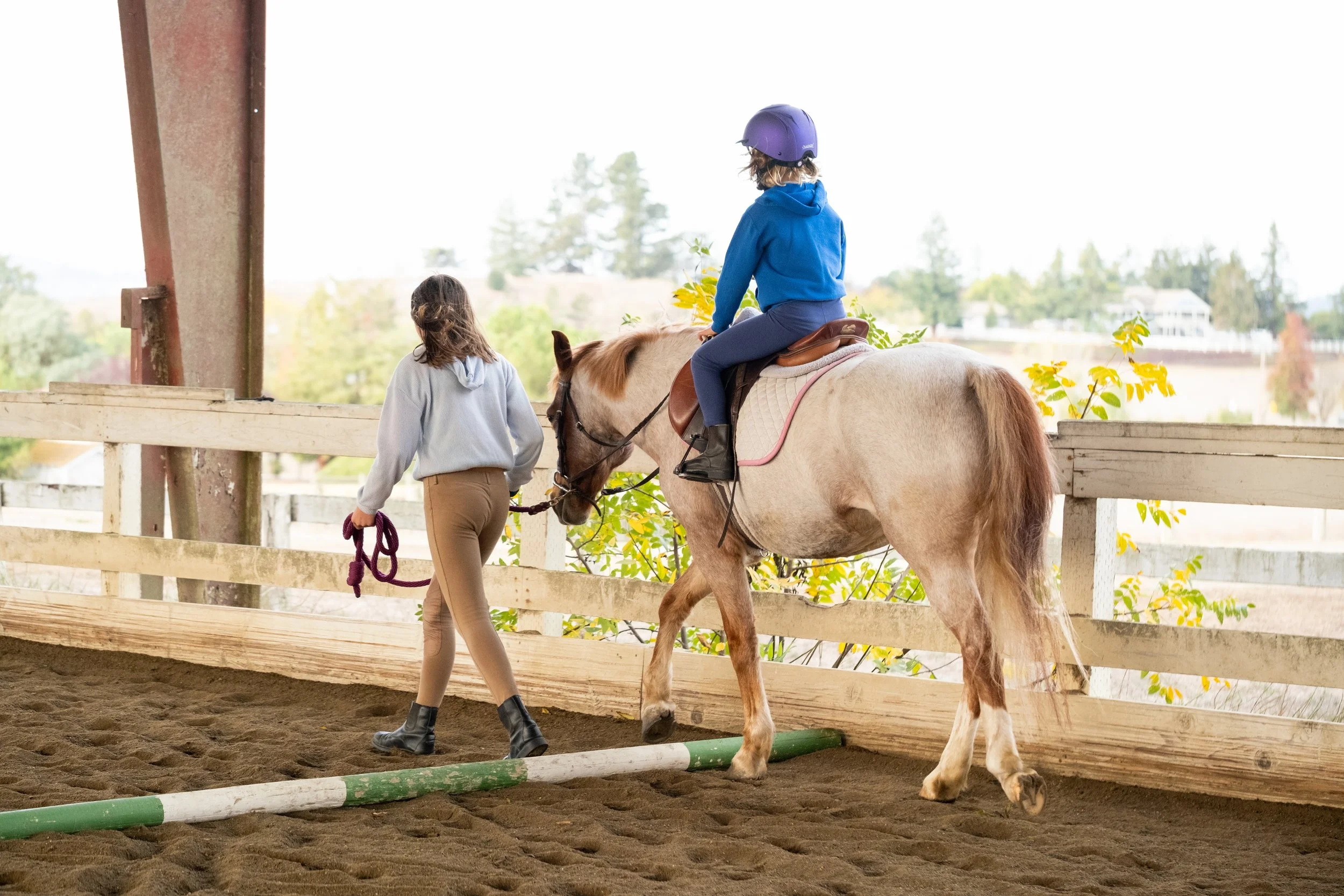 Child riding a horse during a guided lesson at Strides Riding Academy in Sonoma County, led by an instructor inside a covered riding arena.