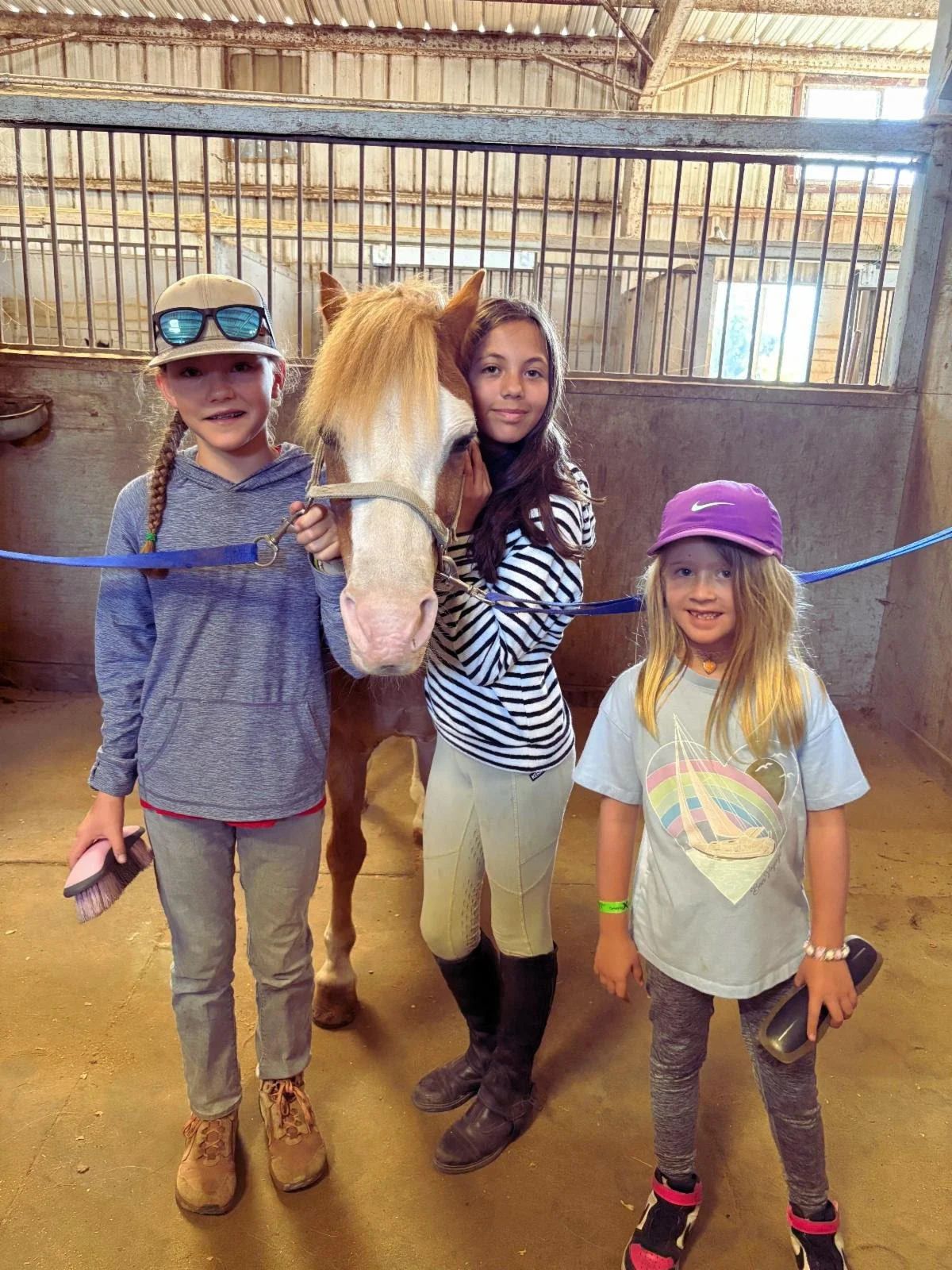 Three smiling young riders bonding with their pony at Strides Riding Academy barn during September lessons.