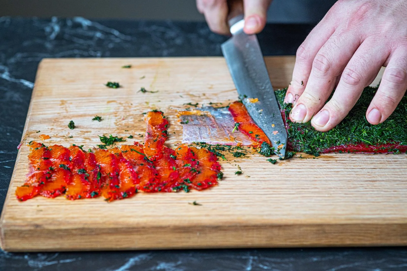 Person chopping herbs on a wooden cutting board with dried tomato slices.