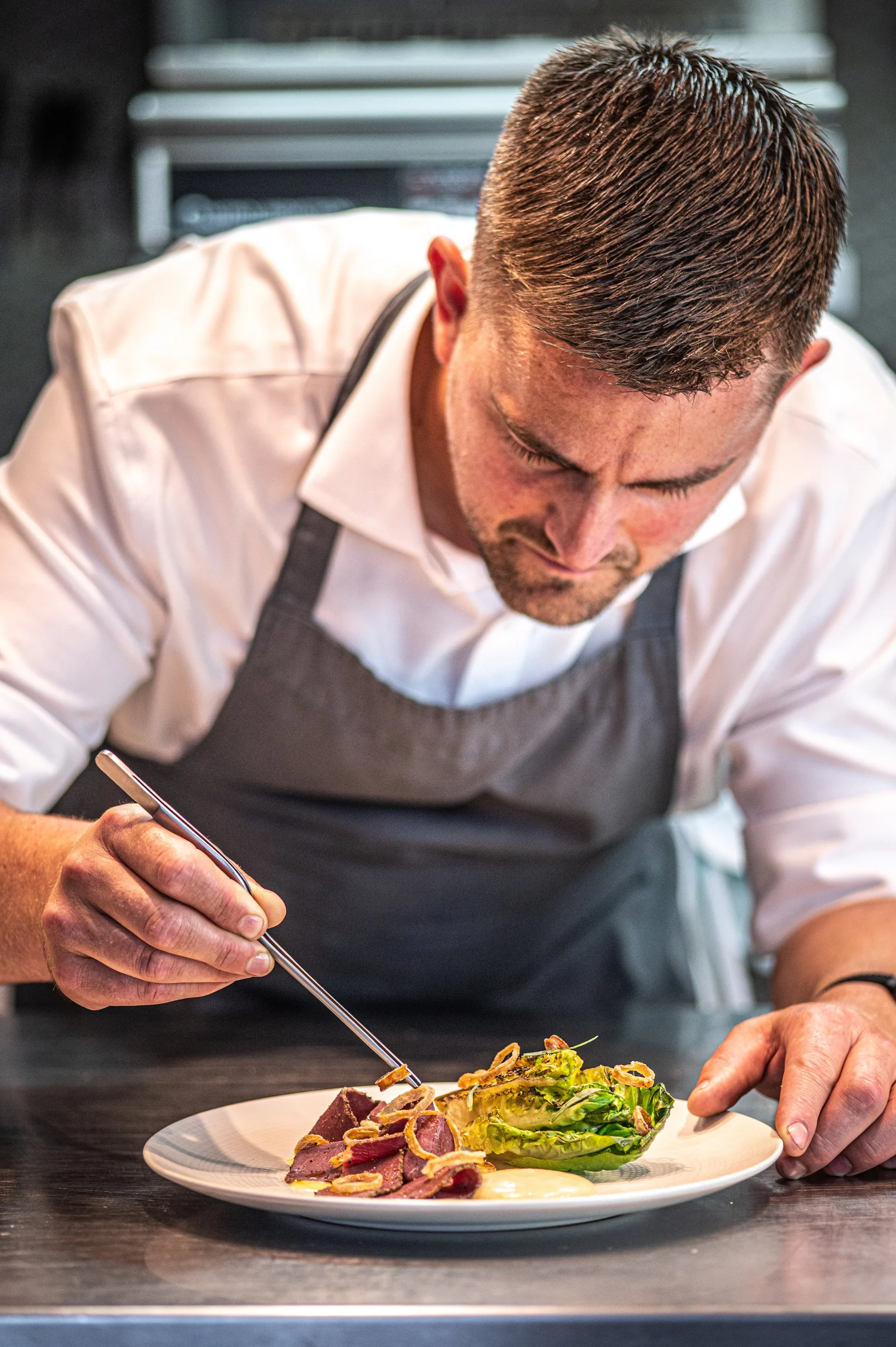 A chef carefully finishing a plate in the YouBeChef restaurant kitchen