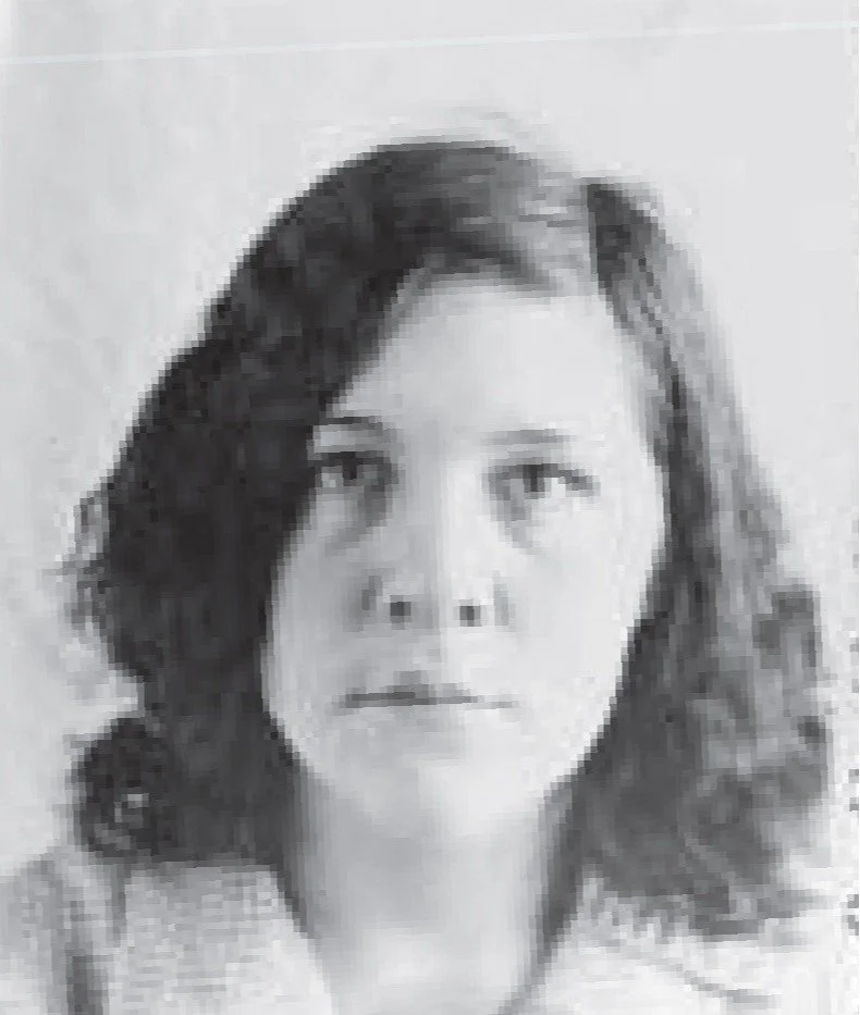 Mildred Strain's mug shots. Mildred is a white woman with shoulder length, slightly curly brown hair. She wears her hair side-parted, with a barrette.  She appears to be wearing a blouse and sweater. She has slight circles under her eyes.