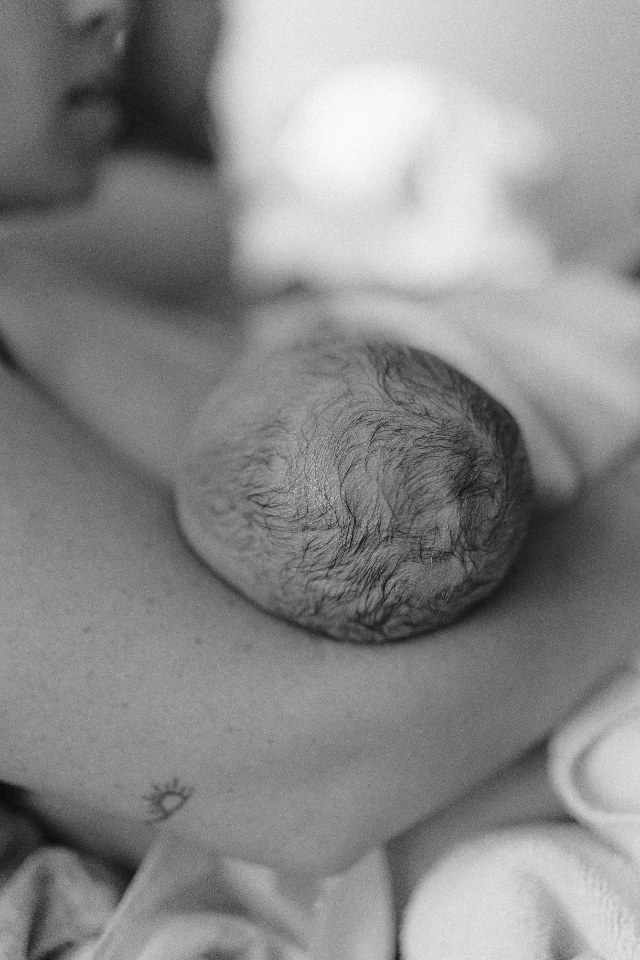 Close-up of a newborn baby's face and head, lying down, with a focus on hair and skin detail, in black and white.