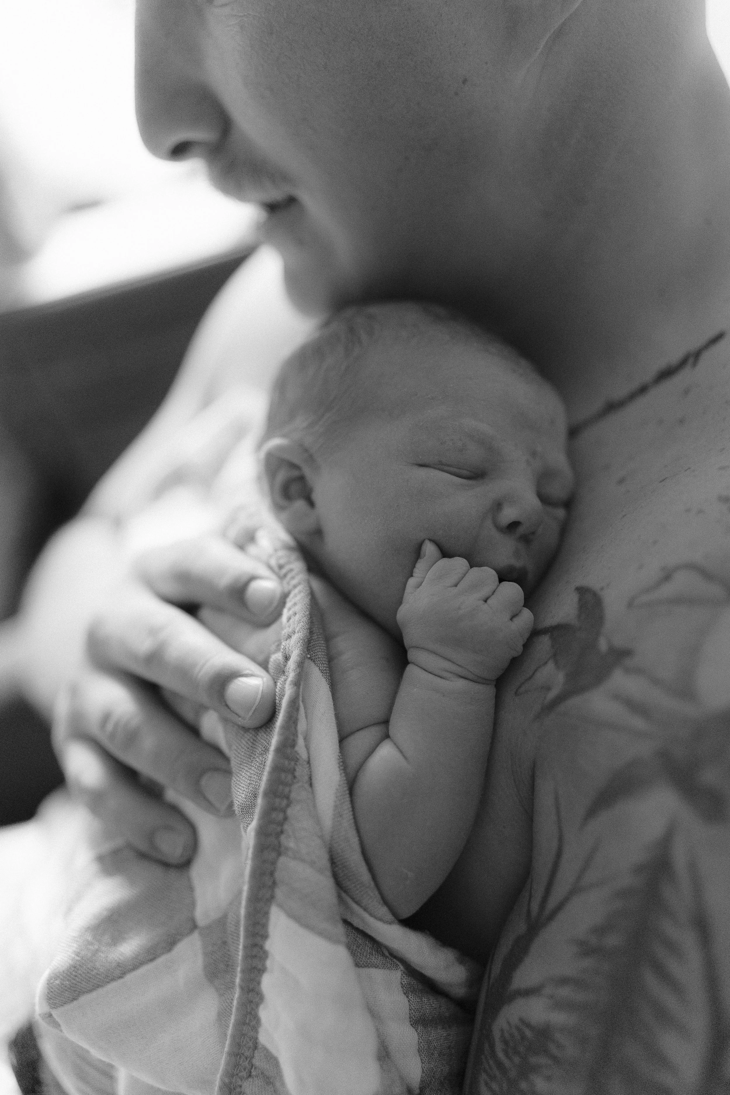 Close-up of a person holding a sleeping newborn baby, with the baby's hand near its face, in black and white.