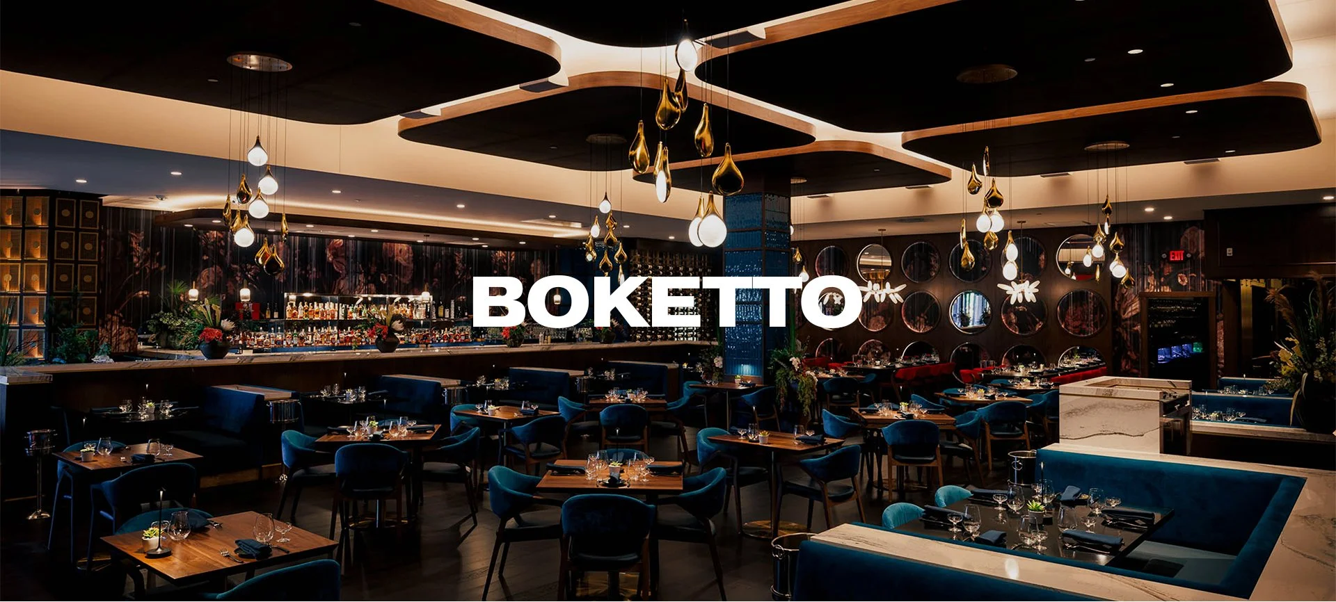 Interior of a modern upscale restaurant with dark wood accents, blue upholstered chairs, a well-stocked bar, and contemporary lighting fixtures.