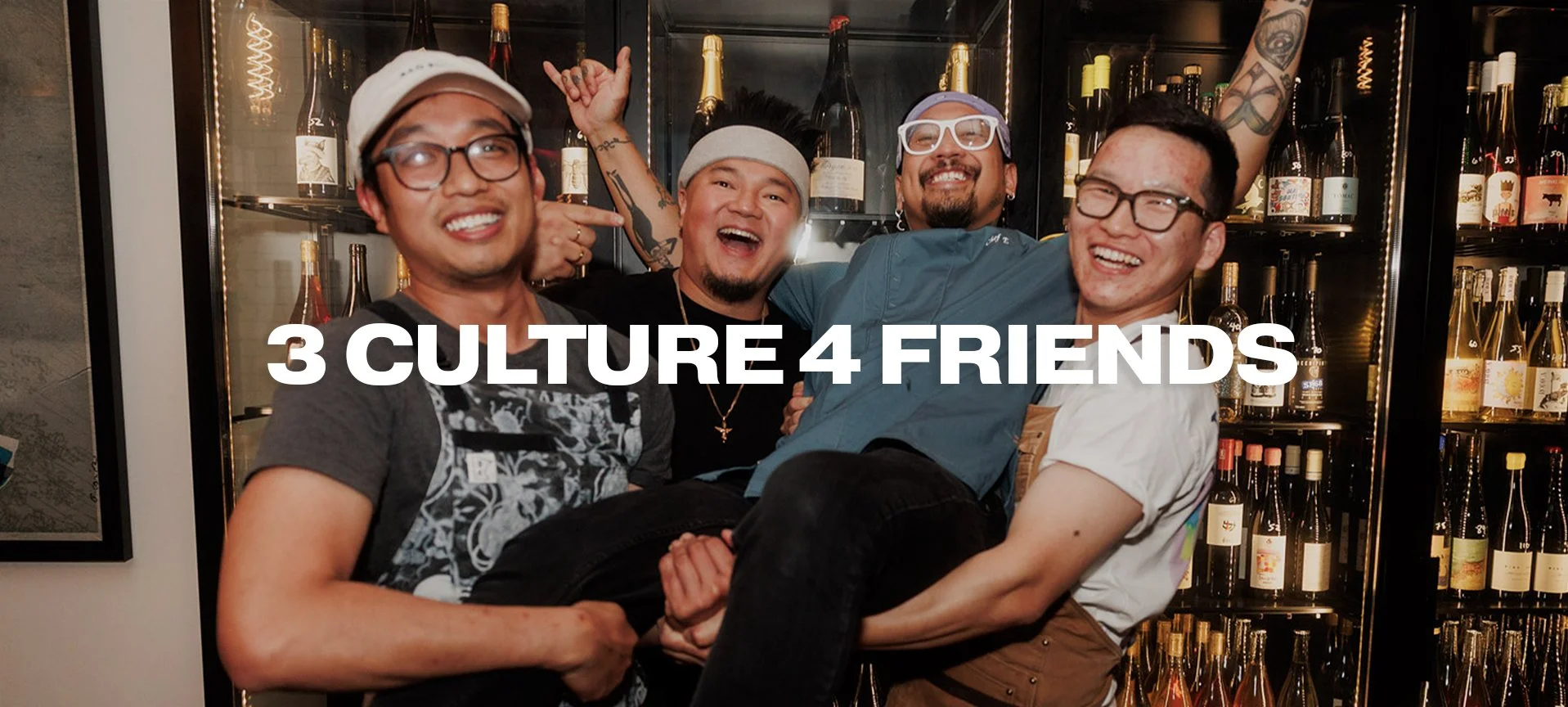 Group of four diverse friends laughing and smiling at a bar, with bottles of wine on shelves in the background, celebrating friendship and cultural diversity.