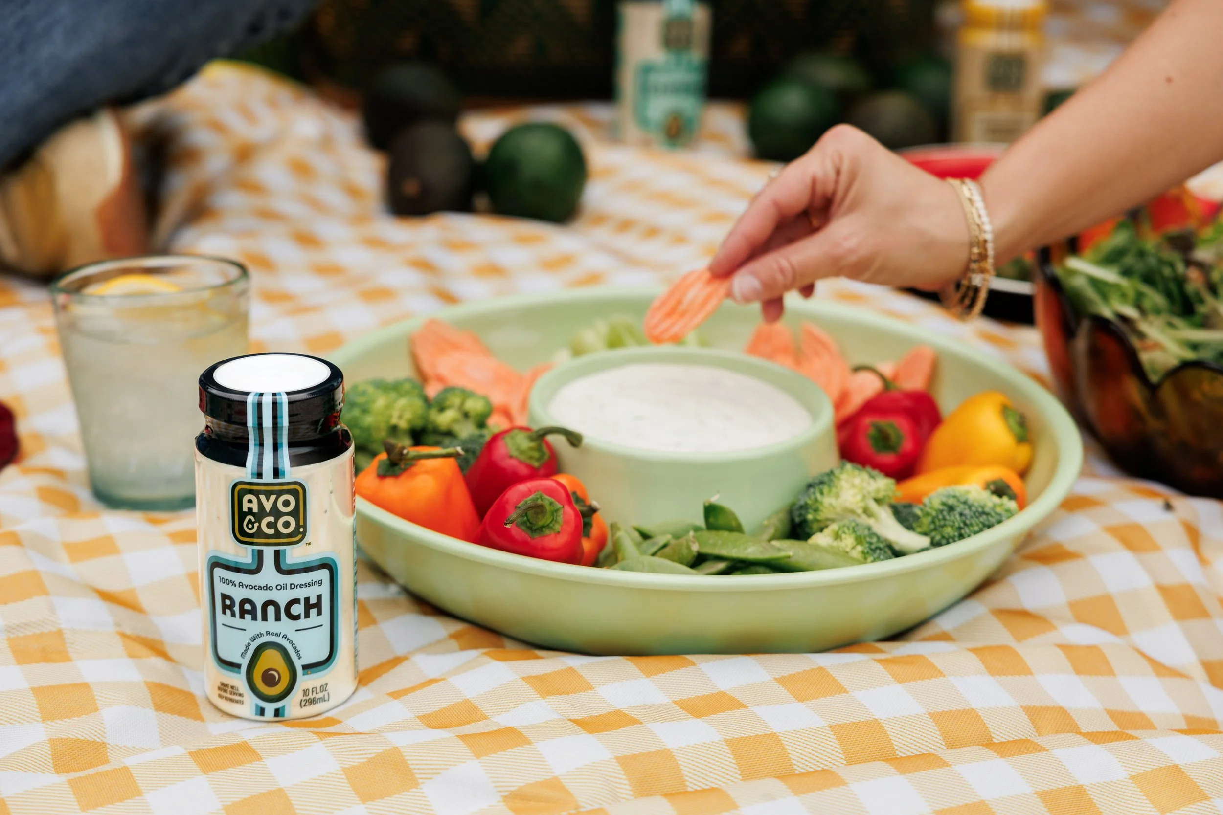 Brand photos showing the product in use, with a person dipping vegetables into salad dressing
