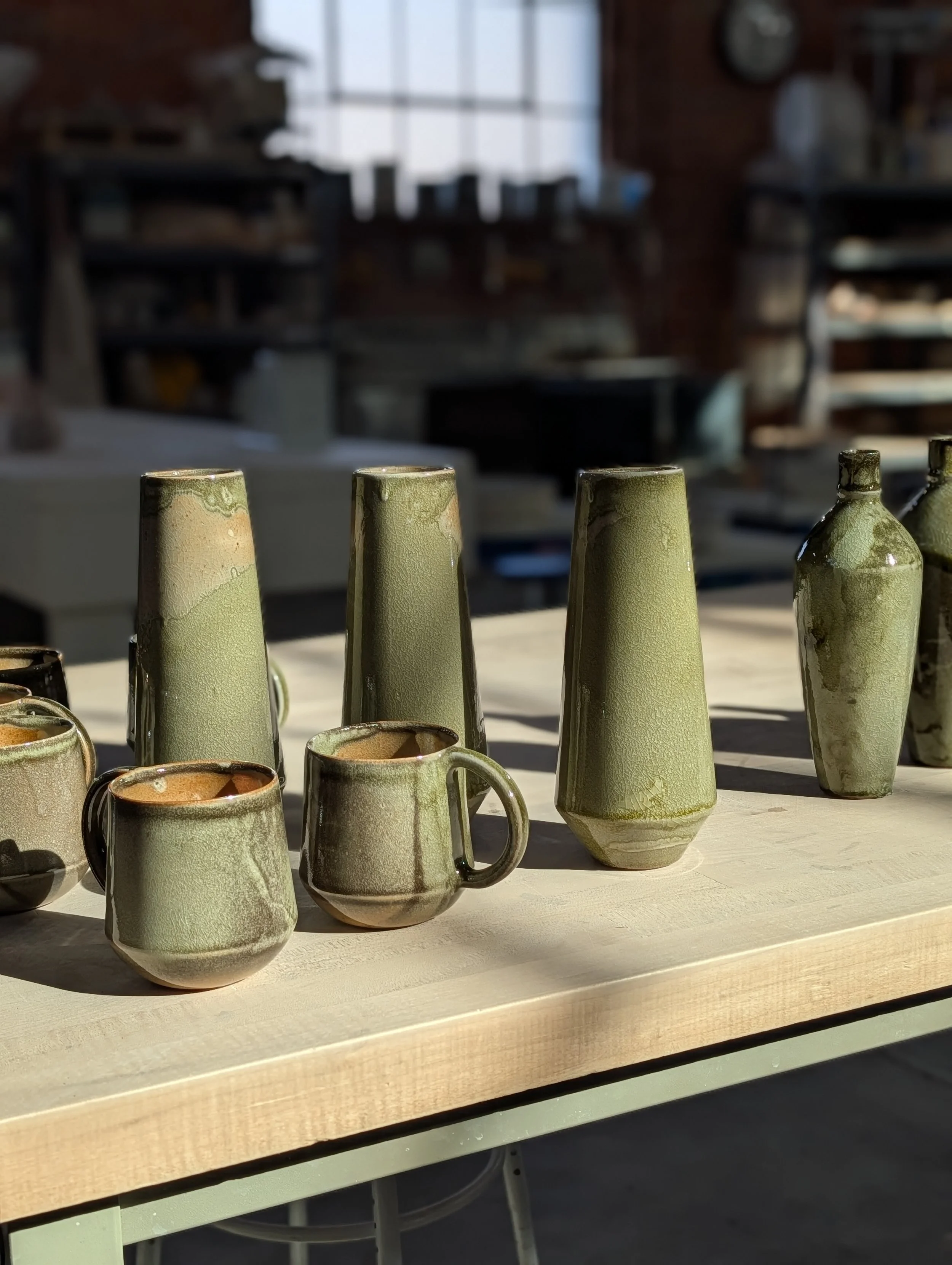 Green Vases, bottles and mugs on a sun-drenched table at new earth ceramics