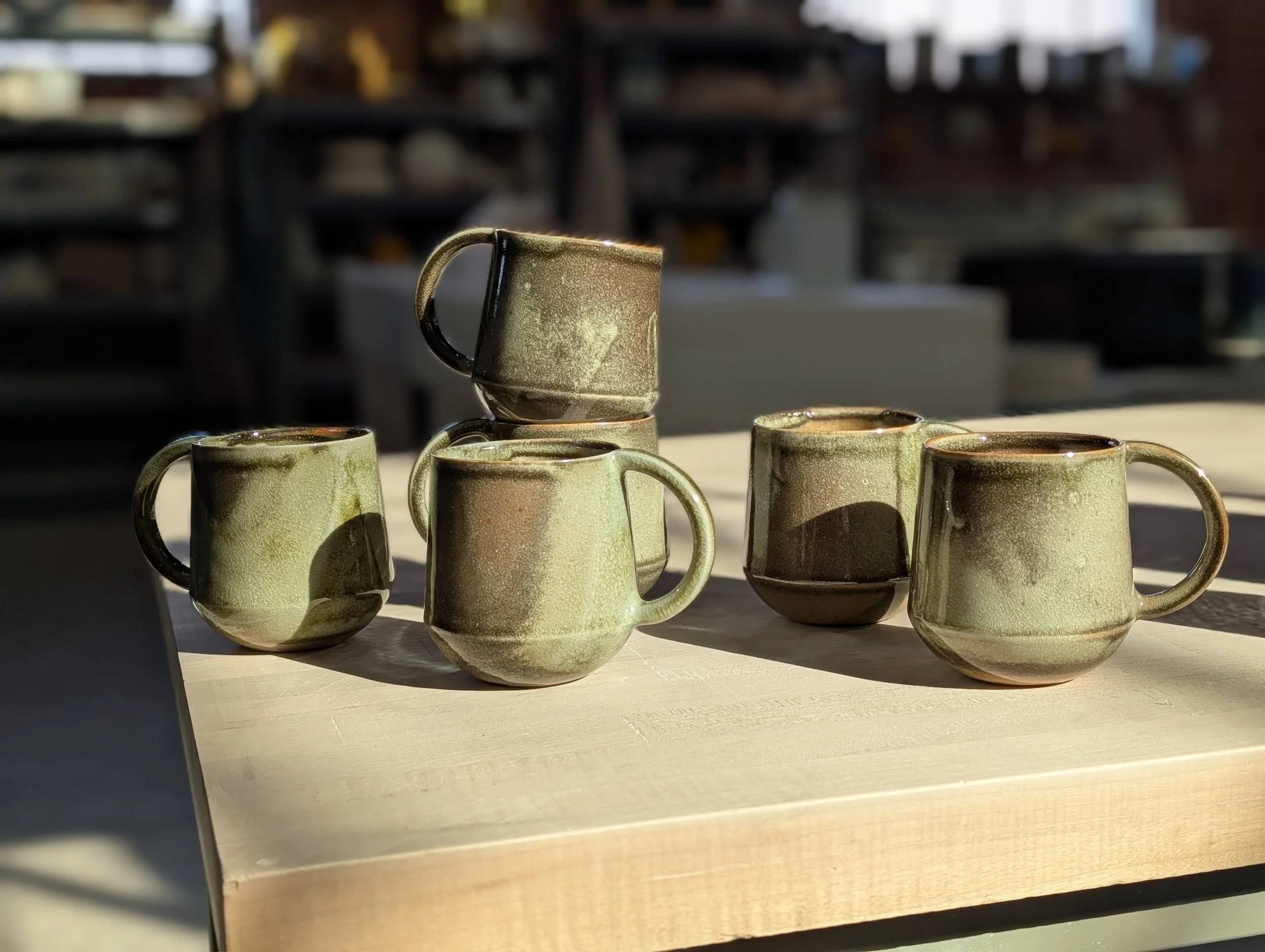 6 green shino mugs scattered across a studio table at new earth ceramics