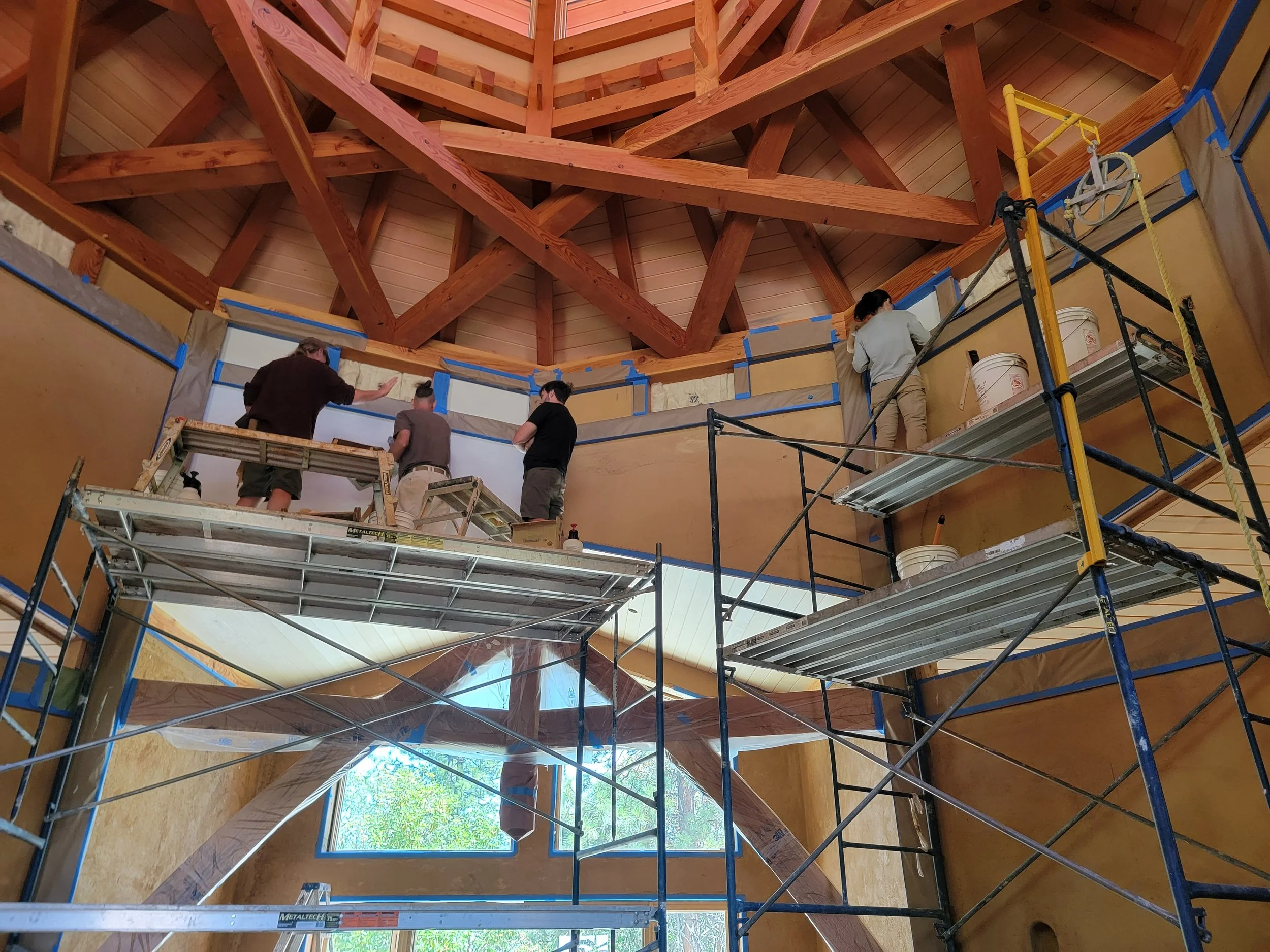 Construction workers working on scaffolding inside a building with wooden beams and a large window.