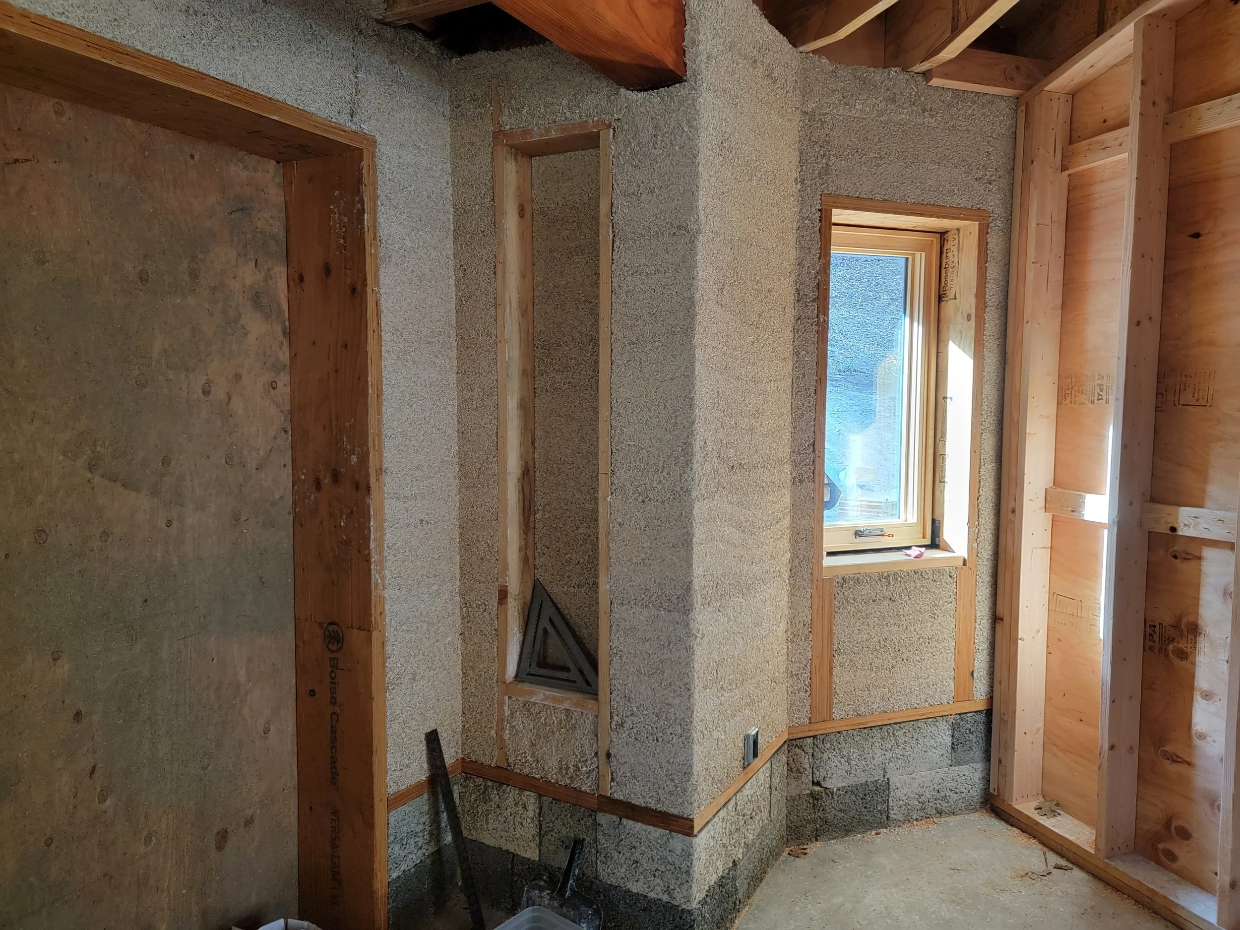 Interior of a room under construction with exposed wooden framing, insulation, and a window letting in natural light.