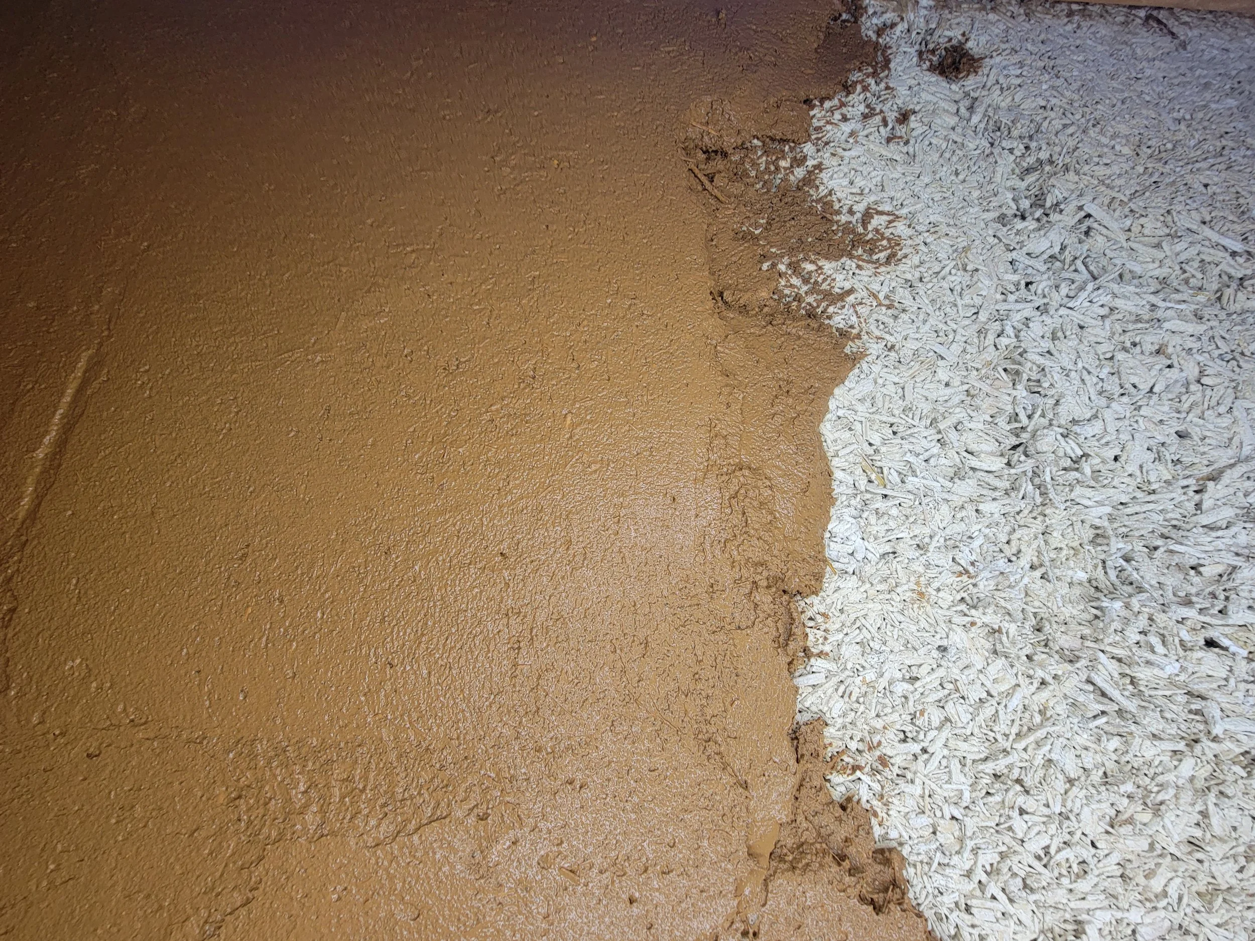 Close-up of a textured wall with a crack, partially painted brown, with white shredded insulation or foam around the edges.