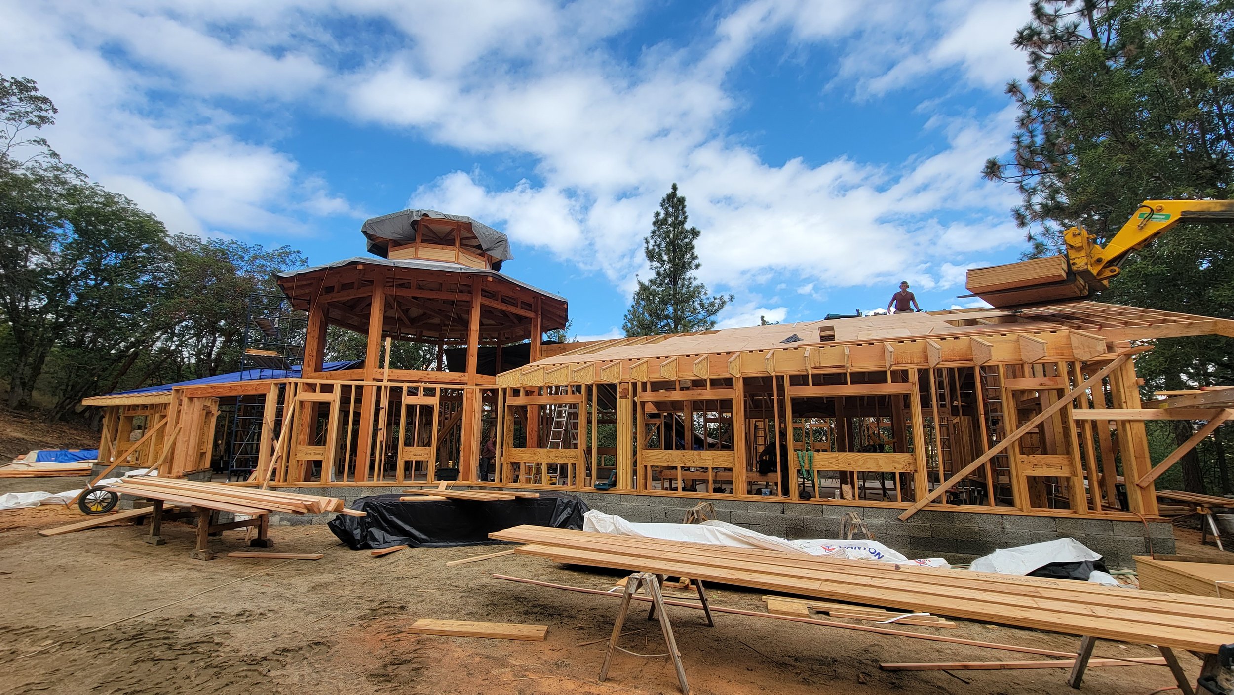 Construction of a wooden house with framing, scaffolding, and construction tools outdoors under a partly cloudy sky.