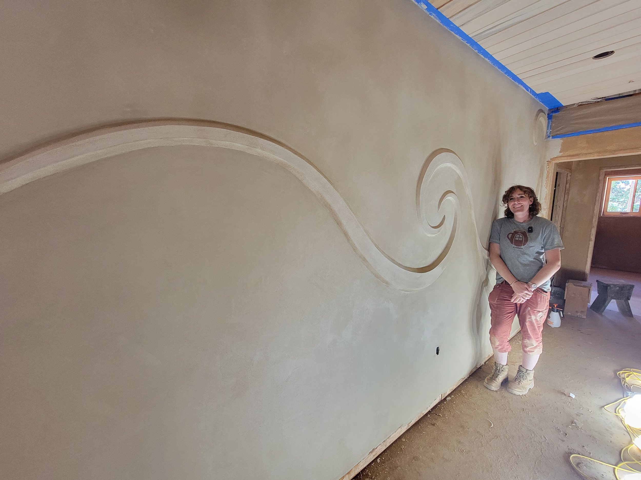 A woman standing next to a wall with swirl painted texture, under construction with blue painter's tape and tools nearby.
