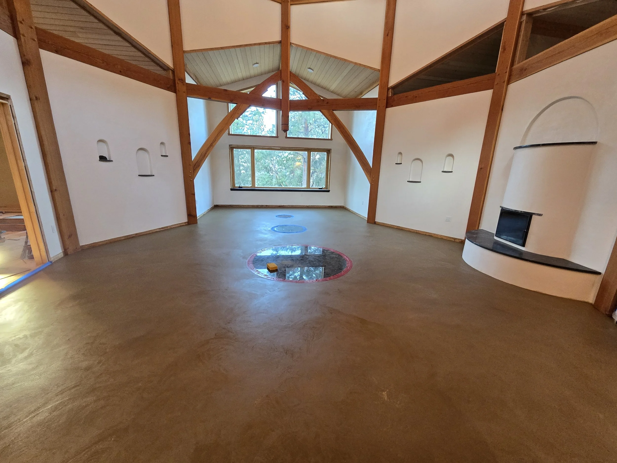 Empty living room with high vaulted ceiling, large window, wooden beams, and a white fireplace with a black mantel.