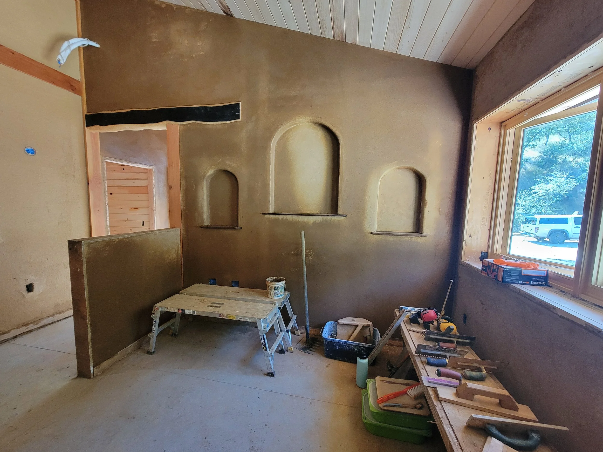 Interior of a room under construction with built-in wall niches, a window with a view outside, and tools on a workbench.