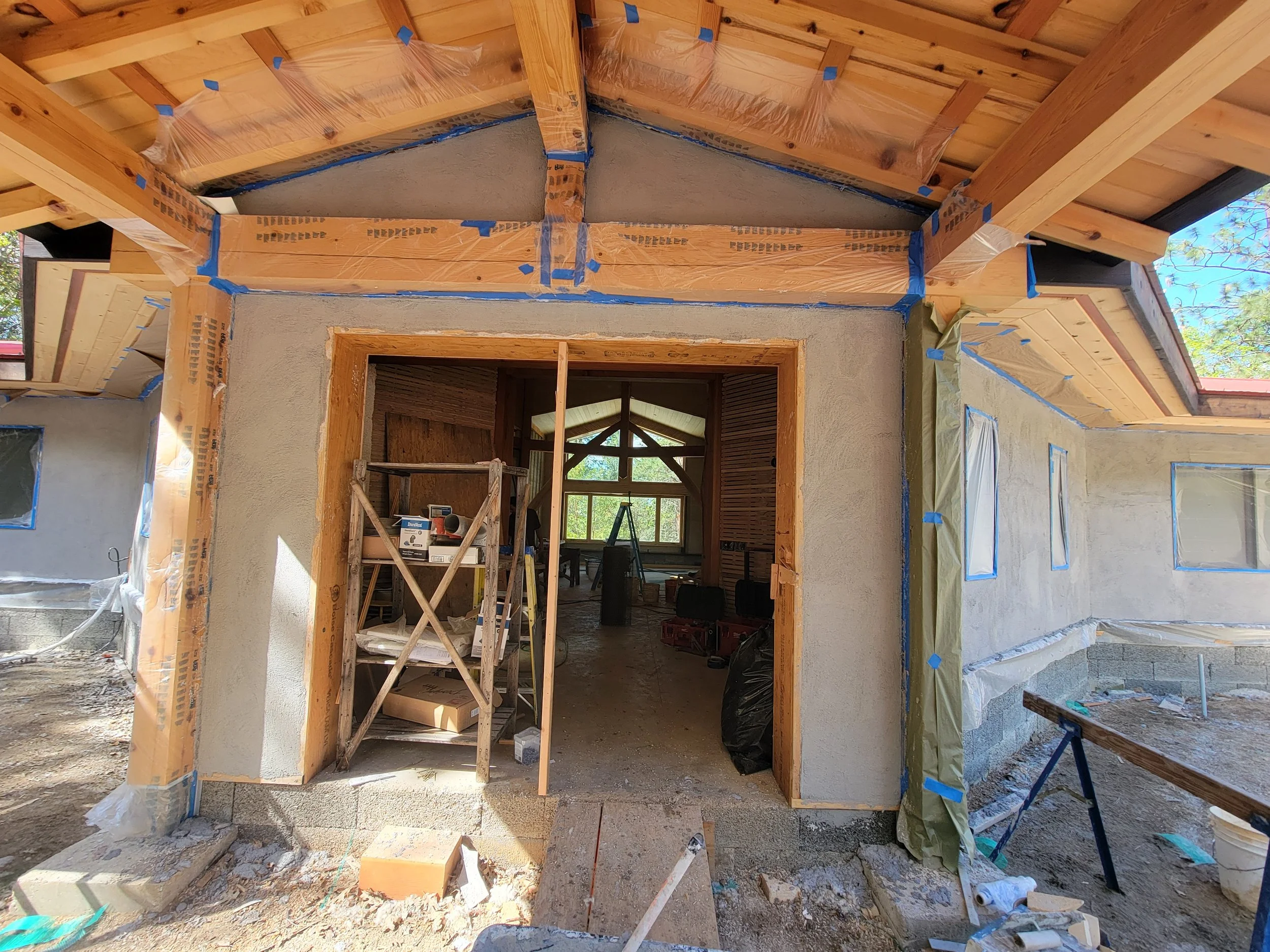 Under construction home exterior with scaffolding, wood framing, and partially finished exterior walls, showing an entryway and windows.