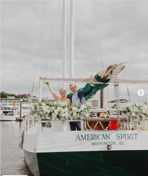 Bride and groom on a boat decorated with flowers, celebrating their wedding, with a man performing a handstand.