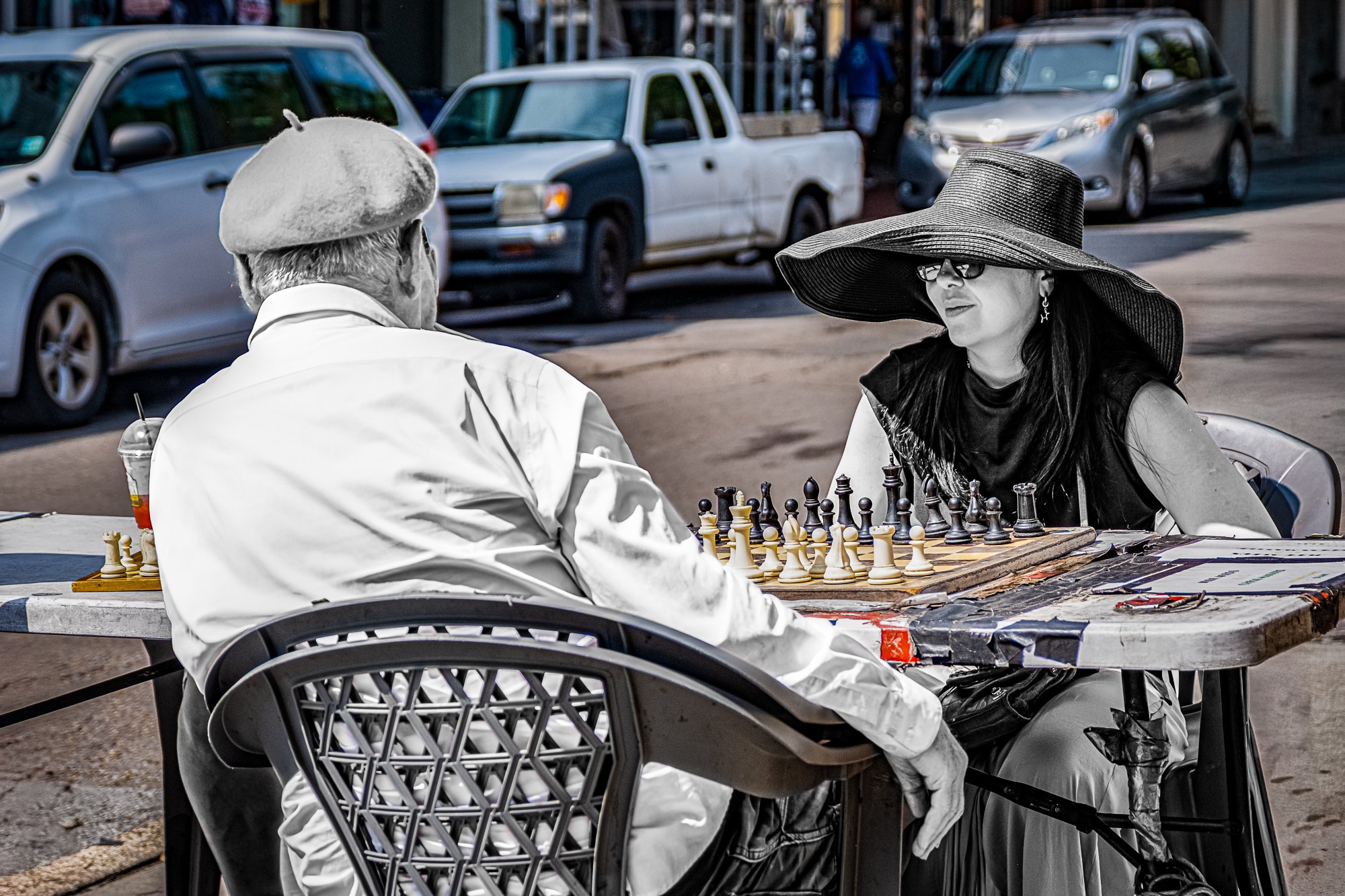 Outside the French Market, a man and woman face off over a chessboard in full sun. No timer, no trash talk—just quiet focus while the crowd flows past. Tourists squeeze by, vendors shout over each other, but these two are locked in. In the middle of