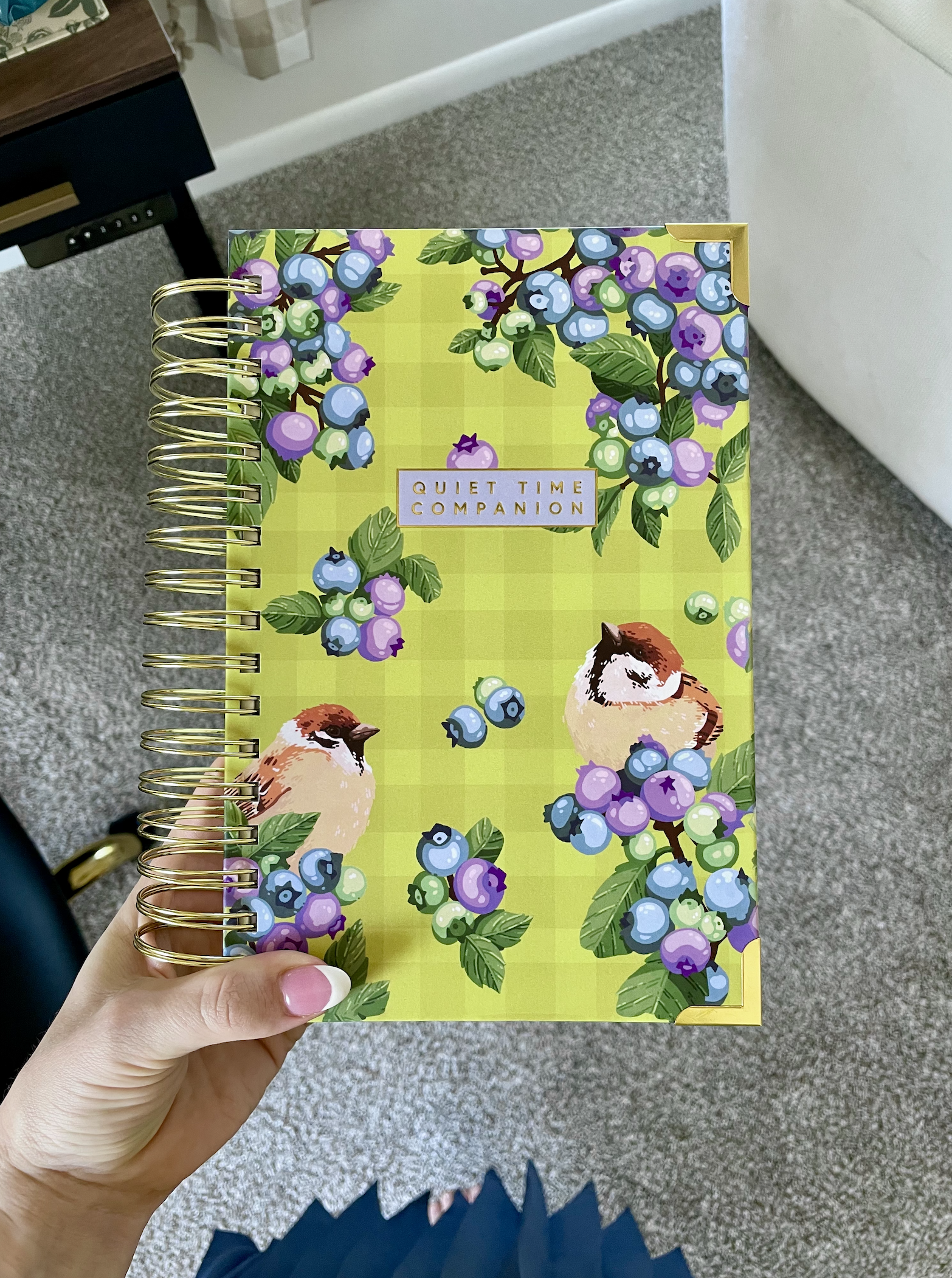 A colorful spiral-bound planner with a cover decorated with blueberries, green leaves, and two birds on a green checkered background. The cover has a label that reads 'Quiet Time Companion.'