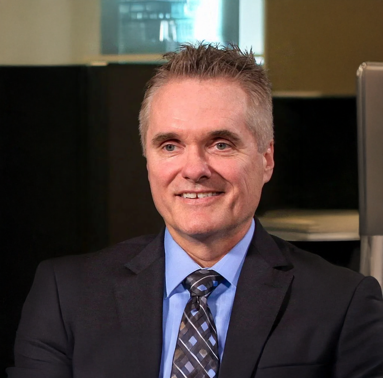 A smiling man in a business suit and tie, in an office setting.