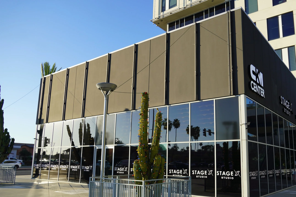 Exterior of a building with reflective glass windows, featuring the sign 'Stage X Studio' and a cactus statue in front.